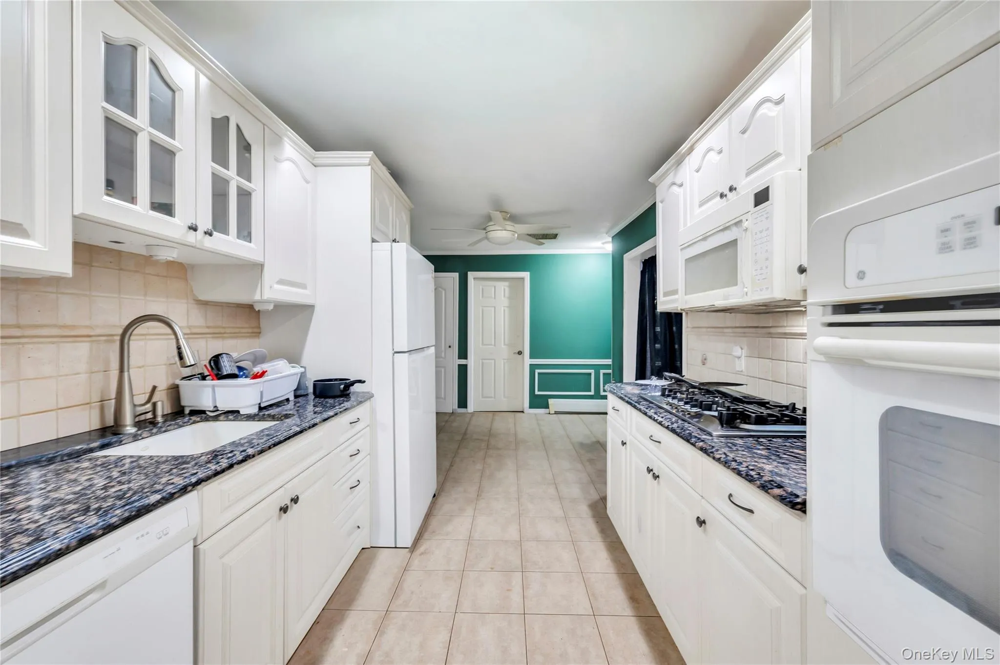Kitchen with backsplash, white appliances, dark stone countertops, white cabinetry, and light tile patterned floors Kitchen with backsplash, white appliances, dark stone countertops, white cabinetry, and light tile patterned floors