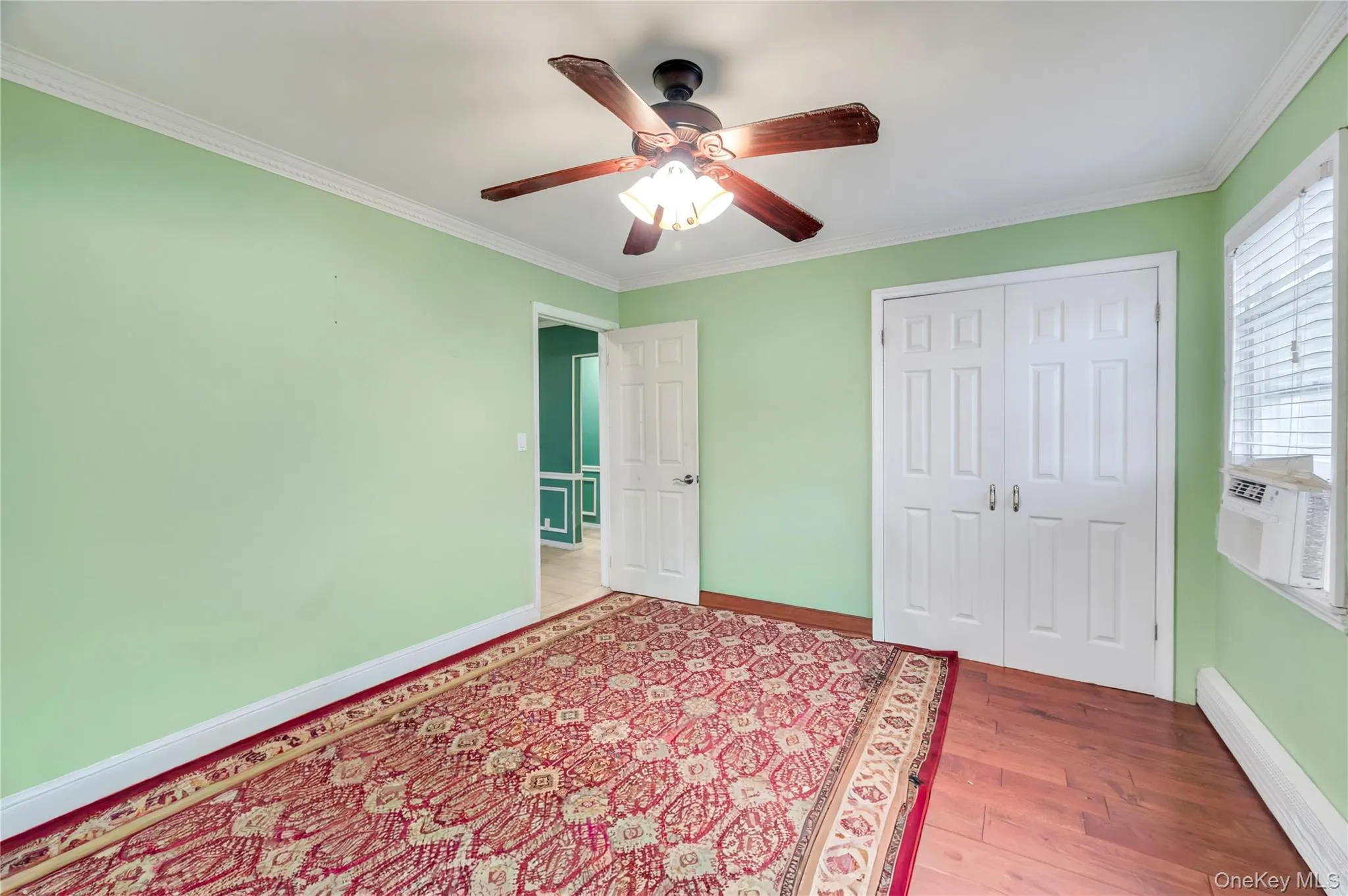Unfurnished bedroom featuring baseboard heating, crown molding, wood finished floors, a ceiling fan, and cooling unit Unfurnished bedroom featuring baseboard heating, crown molding, wood finished floors, a ceiling fan, and cooling unit