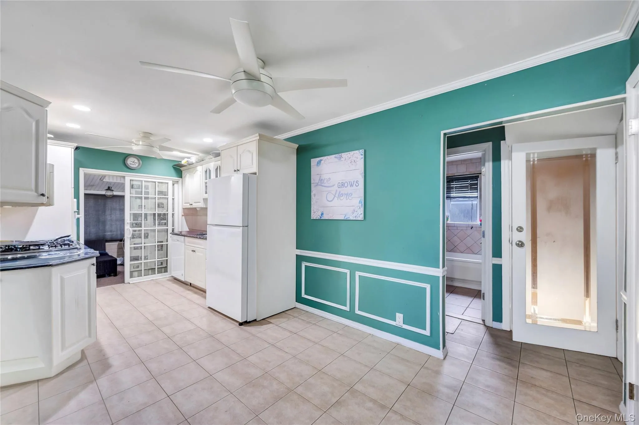 Kitchen featuring light tile patterned flooring, a ceiling fan, white appliances, ornamental molding, and white cabinetry Kitchen featuring light tile patterned flooring, a ceiling fan, white appliances, ornamental molding, and white cabinetry
