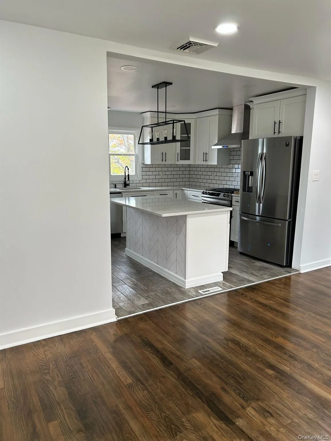 Kitchen featuring appliances with stainless steel finishes, dark wood-type flooring, white cabinetry, decorative backsplash, and wall chimney exhaust hood Kitchen featuring appliances with stainless steel finishes, dark wood-type flooring, white cabinetry, decorative backsplash, and wall chimney exhaust hood