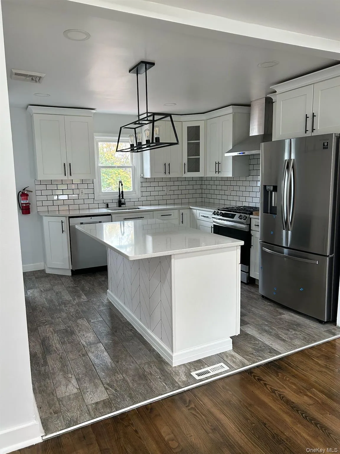 Kitchen featuring stainless steel appliances, white cabinetry, a kitchen island, and backsplash Kitchen featuring stainless steel appliances, white cabinetry, a kitchen island, and backsplash