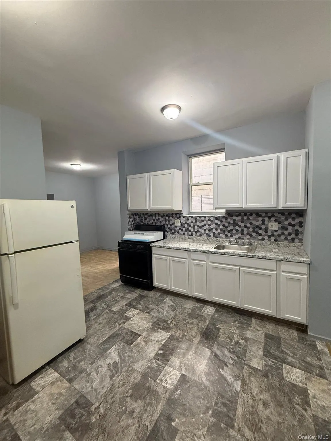 Kitchen featuring freestanding refrigerator, backsplash, black range oven, white cabinets, and dark stone finish flooring Kitchen featuring freestanding refrigerator, backsplash, black range oven, white cabinets, and dark stone finish flooring