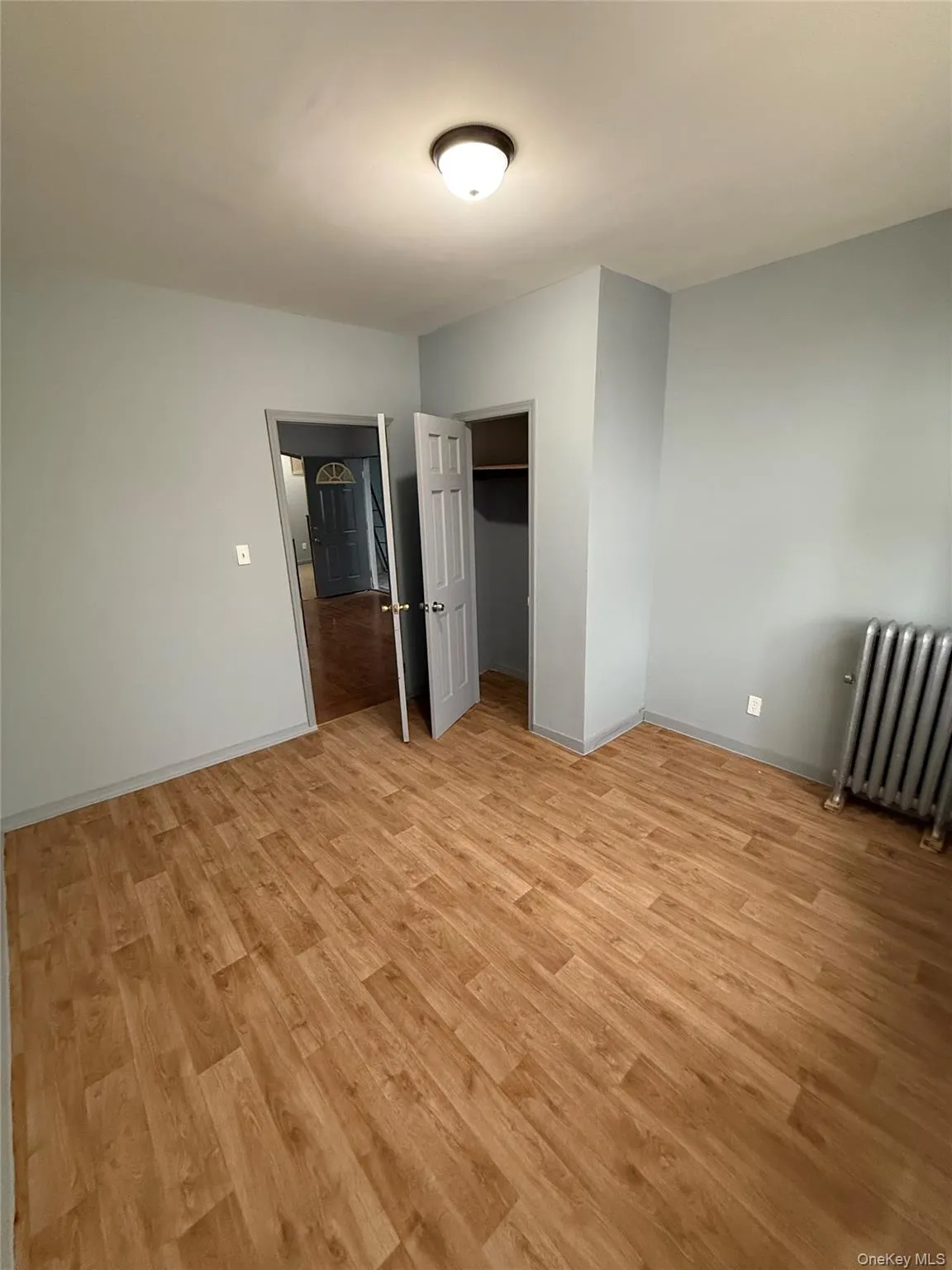 Unfurnished bedroom with radiator, light wood-type flooring, and a spacious closet Unfurnished bedroom with radiator, light wood-type flooring, and a spacious closet