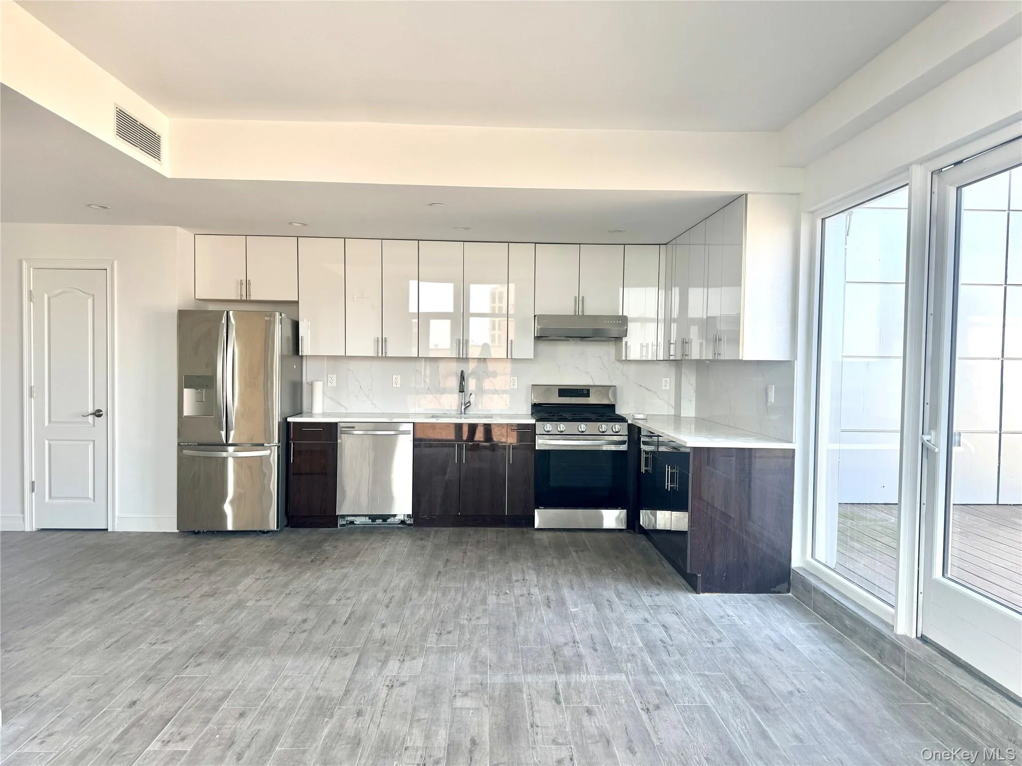 Kitchen with white cabinetry, stainless steel appliances, decorative backsplash, light wood-type flooring, and modern cabinets Kitchen with white cabinetry, stainless steel appliances, decorative backsplash, light wood-type flooring, and modern cabinets
