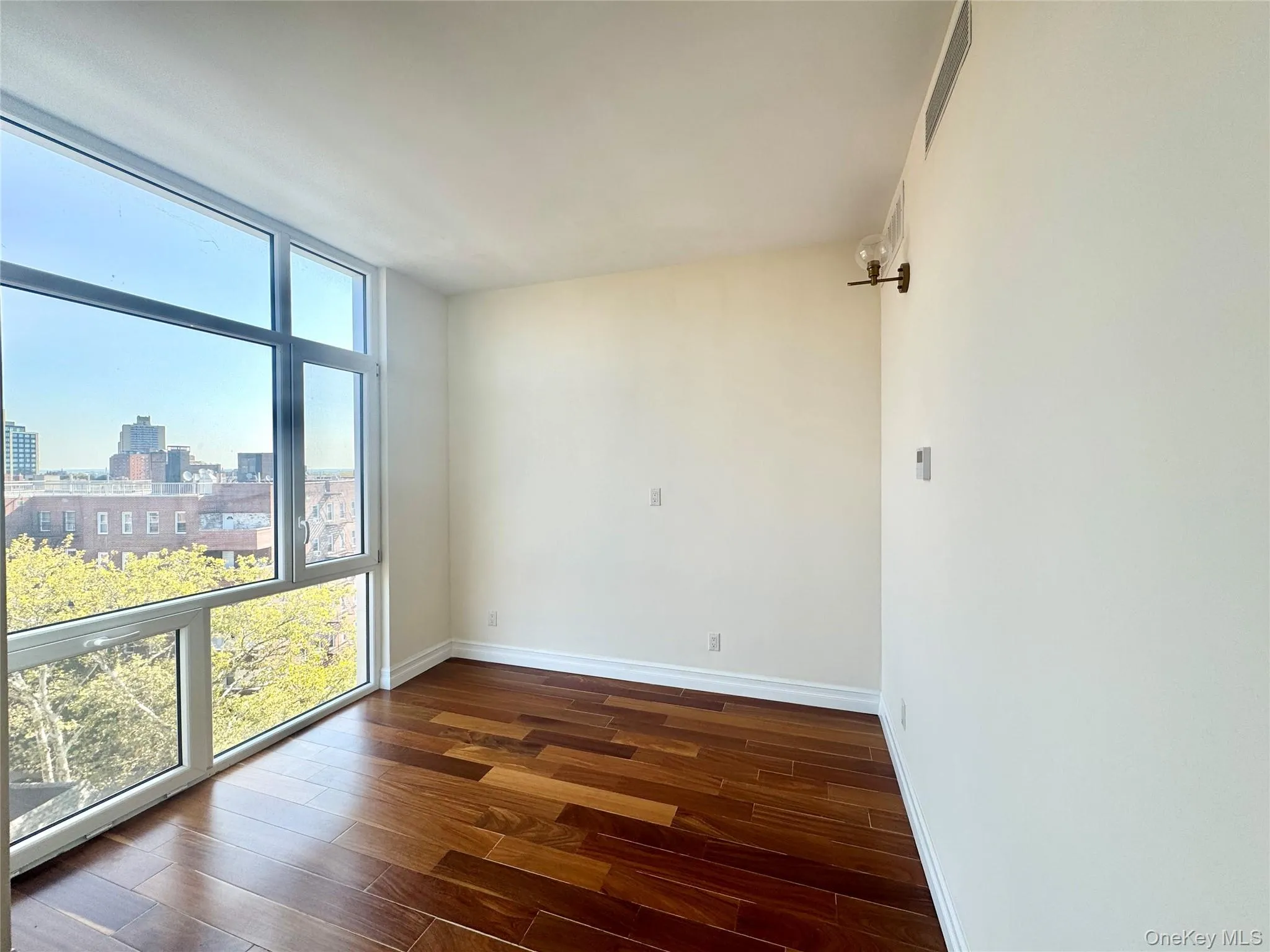 Empty room featuring floor to ceiling windows, dark wood finished floors, and a view of city Empty room featuring floor to ceiling windows, dark wood finished floors, and a view of city