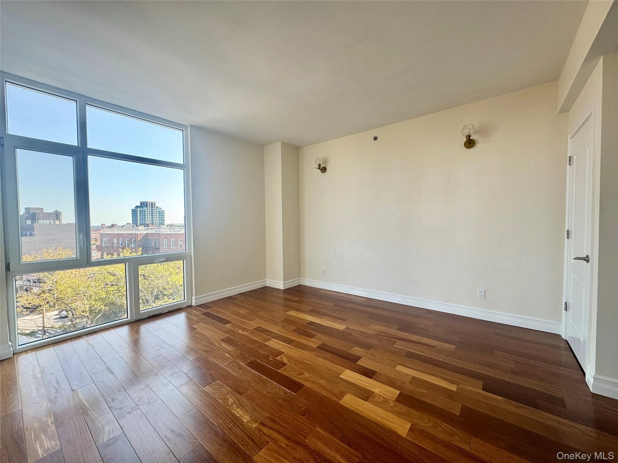 Empty room featuring a wall of windows, dark wood-type flooring, and a view of city Empty room featuring a wall of windows, dark wood-type flooring, and a view of city