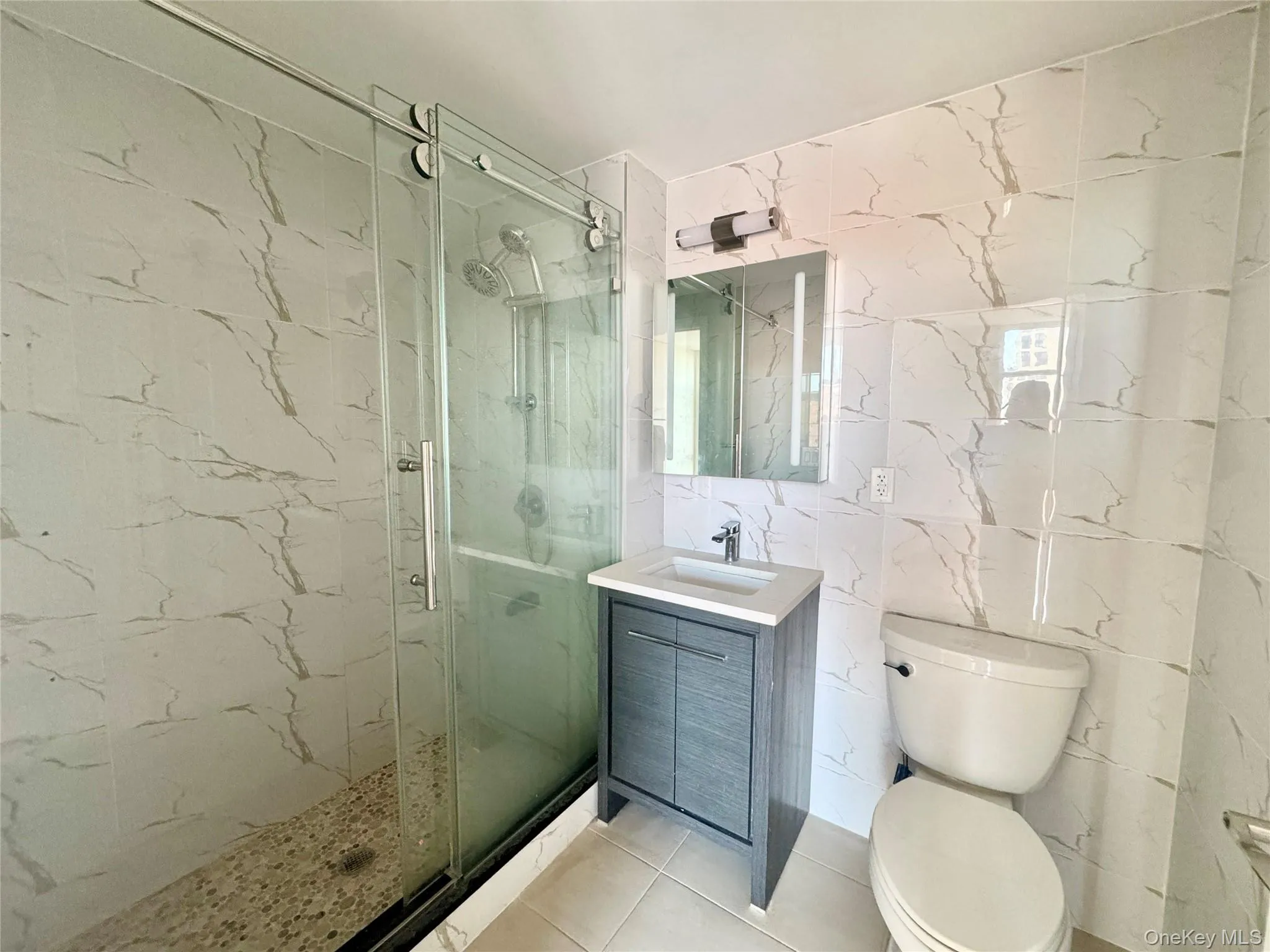 Bathroom featuring vanity, tile walls, a marble finish shower, and light tile patterned floors Bathroom featuring vanity, tile walls, a marble finish shower, and light tile patterned floors
