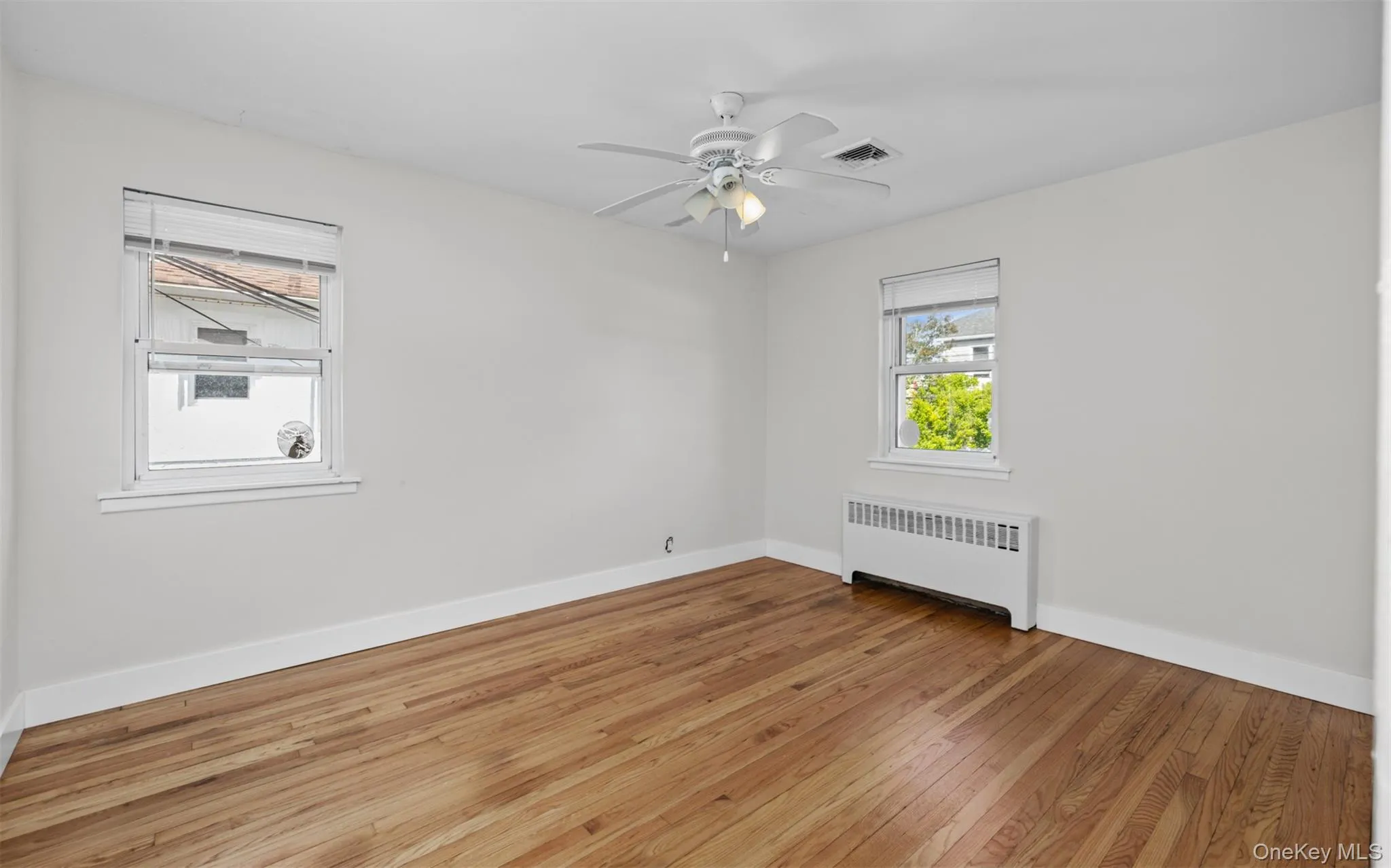 Spare room featuring radiator, light wood finished floors, and a ceiling fan Spare room featuring radiator, light wood finished floors, and a ceiling fan