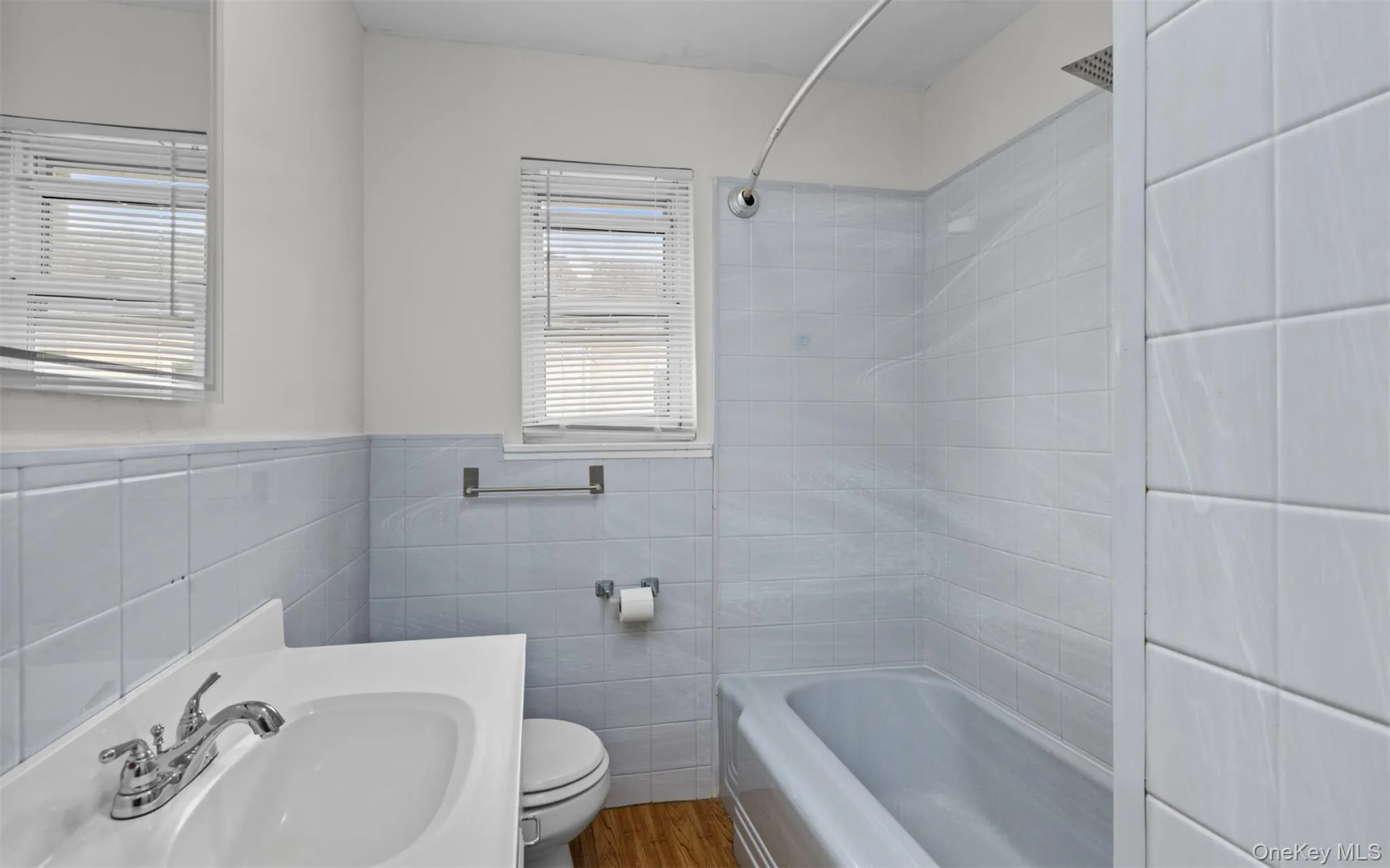 Bathroom featuring tile walls, bathing tub / shower combination, wood finished floors, vanity, and a wainscoted wall Bathroom featuring tile walls, bathing tub / shower combination, wood finished floors, vanity, and a wainscoted wall