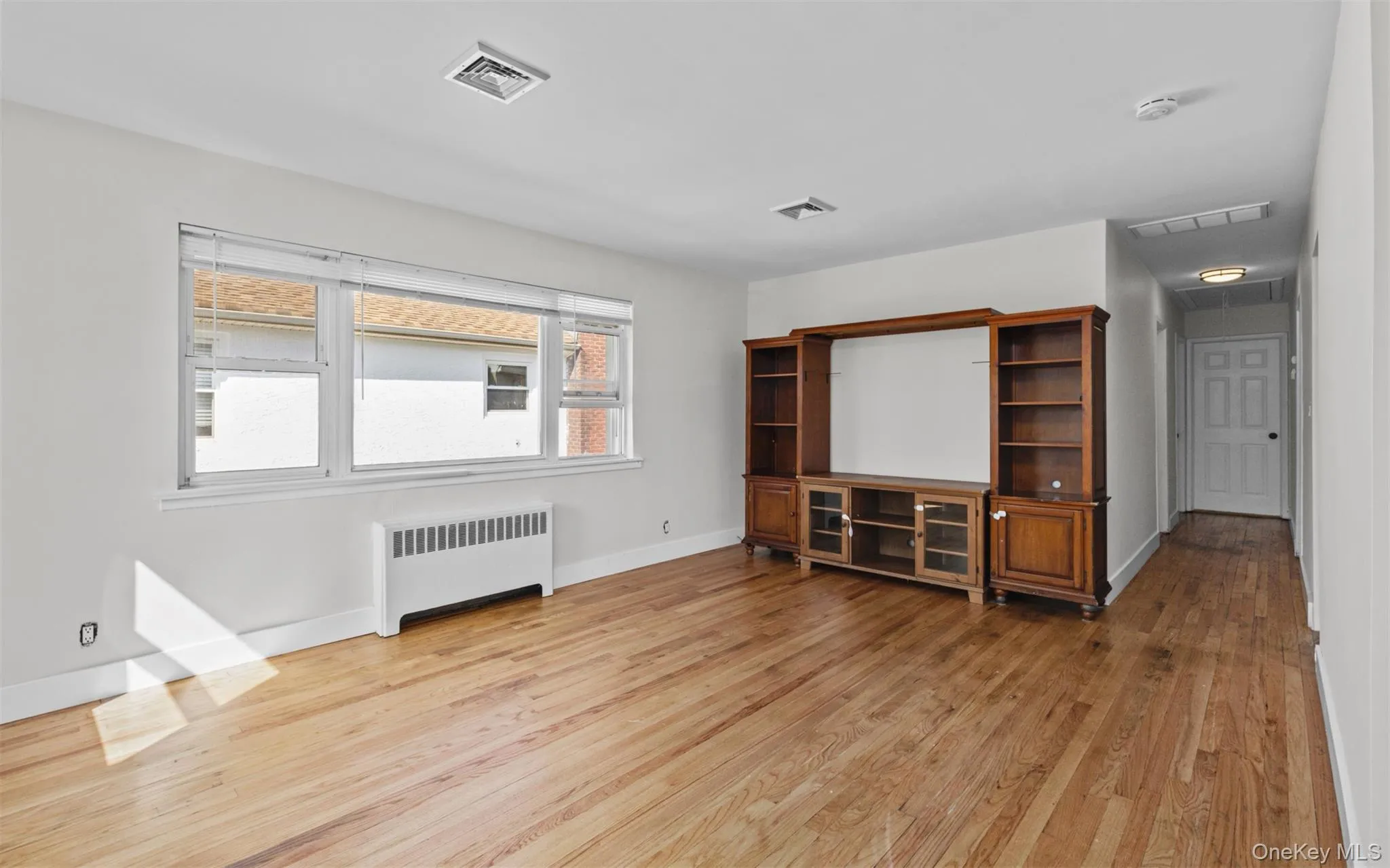Unfurnished living room featuring radiator heating unit and light wood-style floors Unfurnished living room featuring radiator heating unit and light wood-style floors