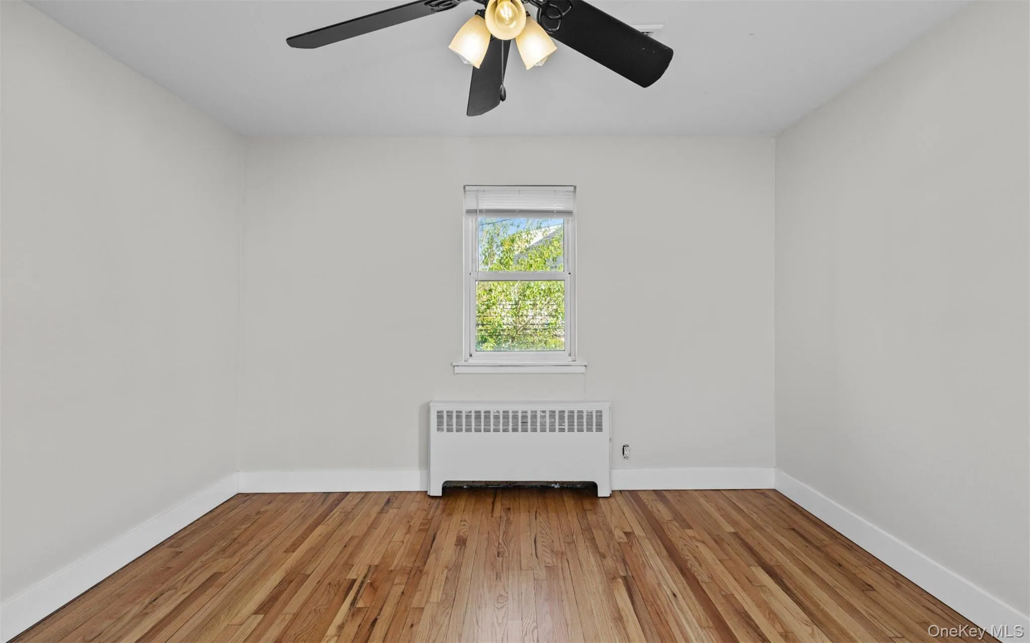 Spare room featuring radiator heating unit and light wood-style floors Spare room featuring radiator heating unit and light wood-style floors