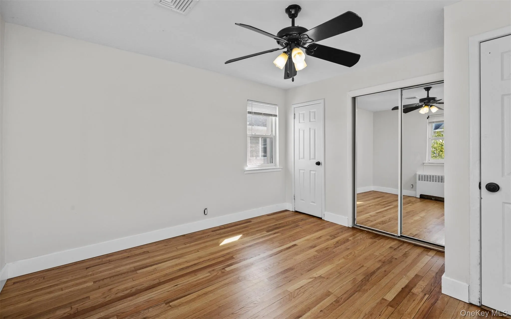 Unfurnished bedroom with light wood finished floors, a ceiling fan, radiator, and a closet Unfurnished bedroom with light wood finished floors, a ceiling fan, radiator, and a closet
