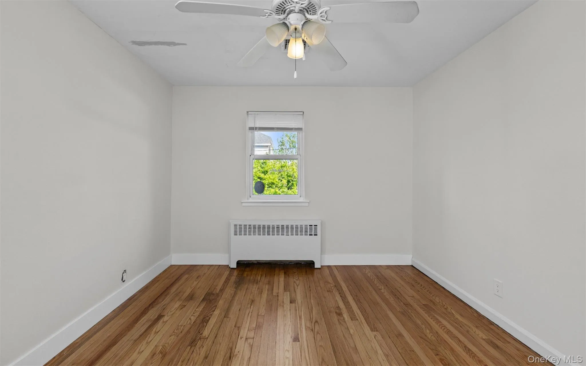 Unfurnished room featuring radiator heating unit, hardwood / wood-style flooring, and ceiling fan Unfurnished room featuring radiator heating unit, hardwood / wood-style flooring, and ceiling fan