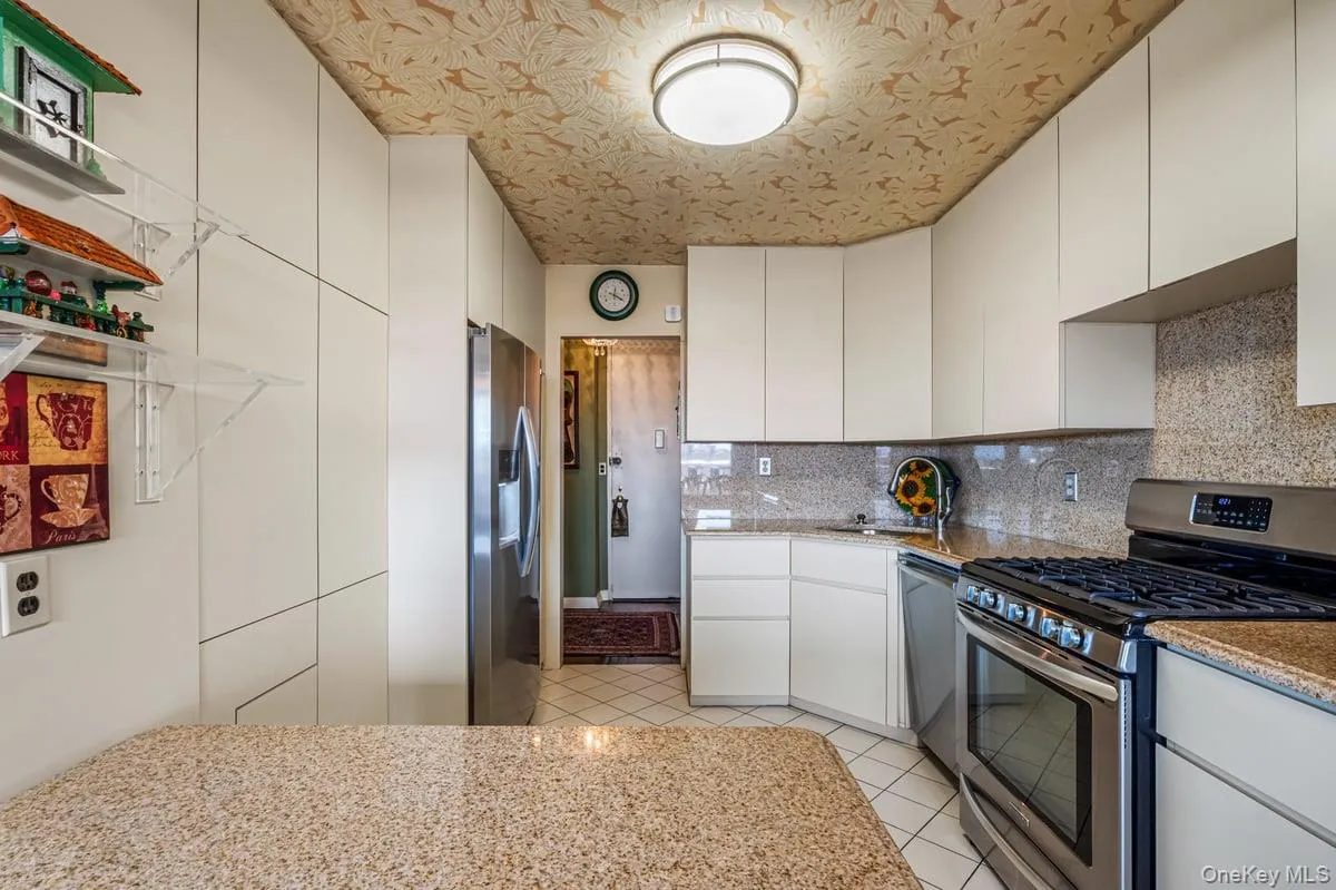 Kitchen featuring appliances with stainless steel finishes, tasteful backsplash, light tile patterned floors, light stone counters, and white cabinetry Kitchen featuring appliances with stainless steel finishes, tasteful backsplash, light tile patterned floors, light stone counters, and white cabinetry