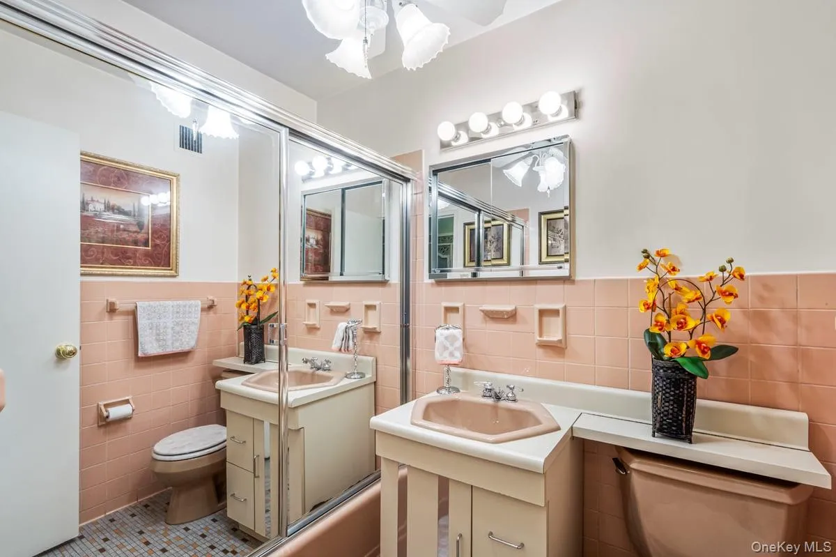 Full bath featuring tile walls, vanity, tile patterned flooring, a wainscoted wall, and bath / shower combo with glass door Full bath featuring tile walls, vanity, tile patterned flooring, a wainscoted wall, and bath / shower combo with glass door