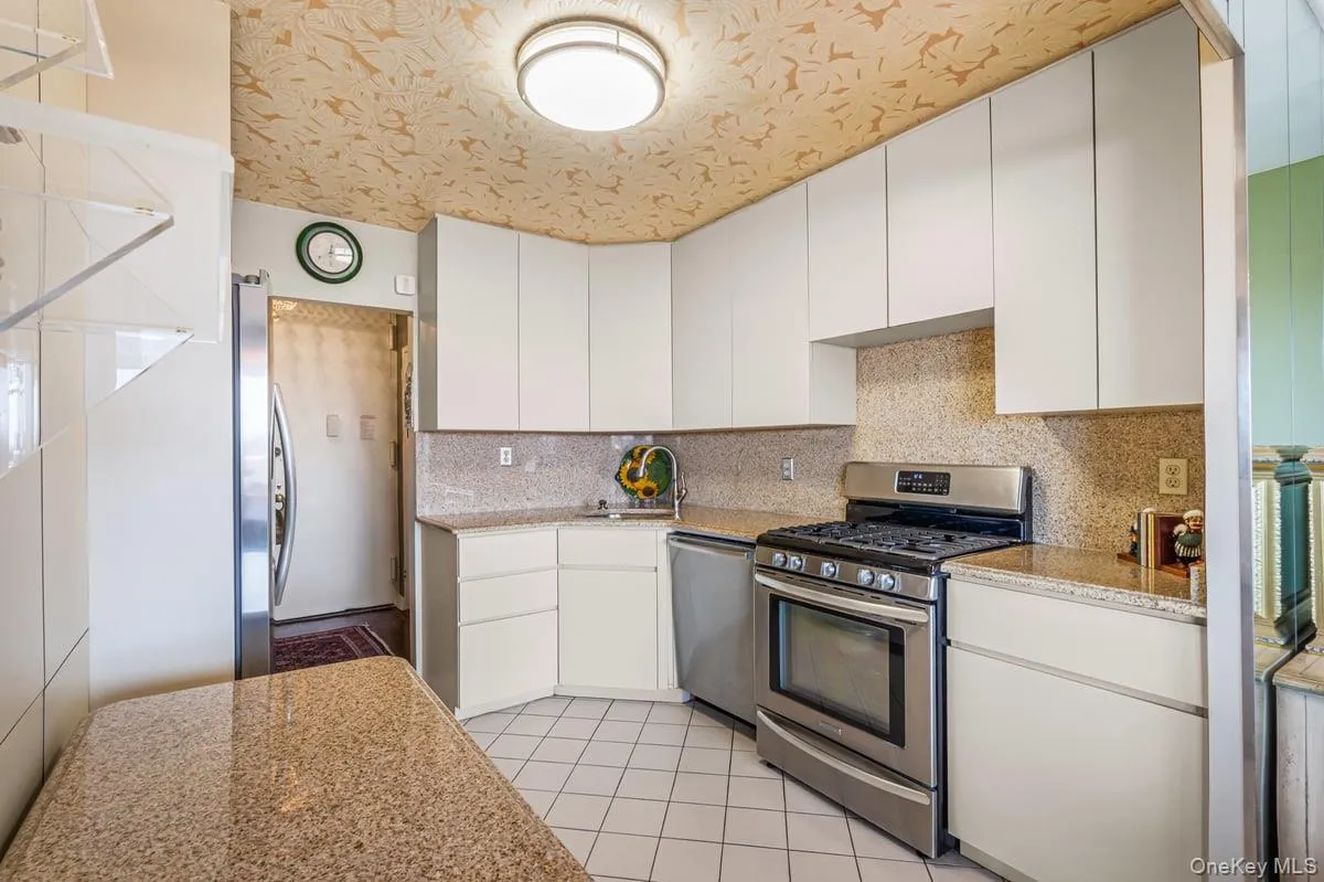 Kitchen with appliances with stainless steel finishes, decorative backsplash, white cabinets, light stone countertops, and light tile patterned floors Kitchen with appliances with stainless steel finishes, decorative backsplash, white cabinets, light stone countertops, and light tile patterned floors