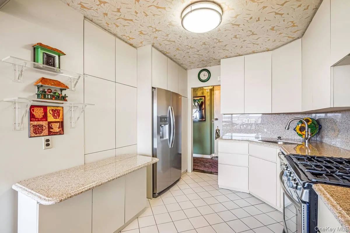 Kitchen with appliances with stainless steel finishes, light stone countertops, light tile patterned floors, white cabinetry, and backsplash Kitchen with appliances with stainless steel finishes, light stone countertops, light tile patterned floors, white cabinetry, and backsplash