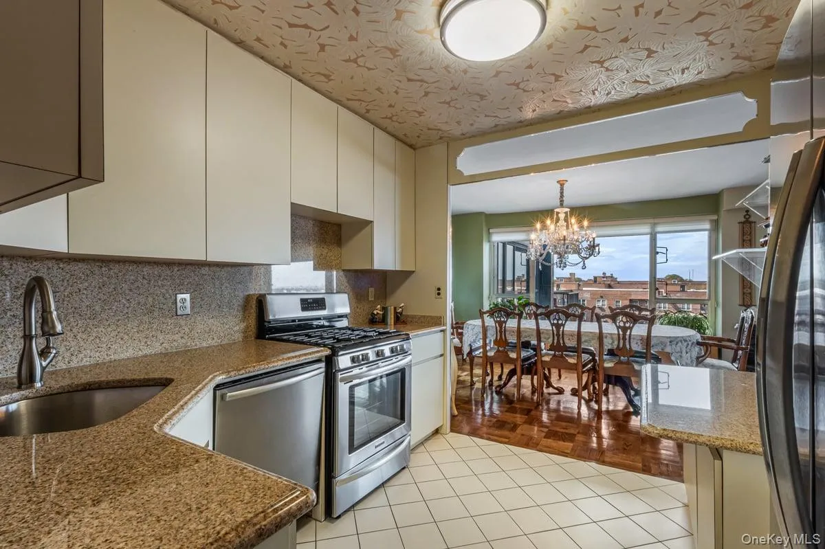 Kitchen with stainless steel appliances, tasteful backsplash, light tile patterned floors, a chandelier, and dark stone countertops Kitchen with stainless steel appliances, tasteful backsplash, light tile patterned floors, a chandelier, and dark stone countertops