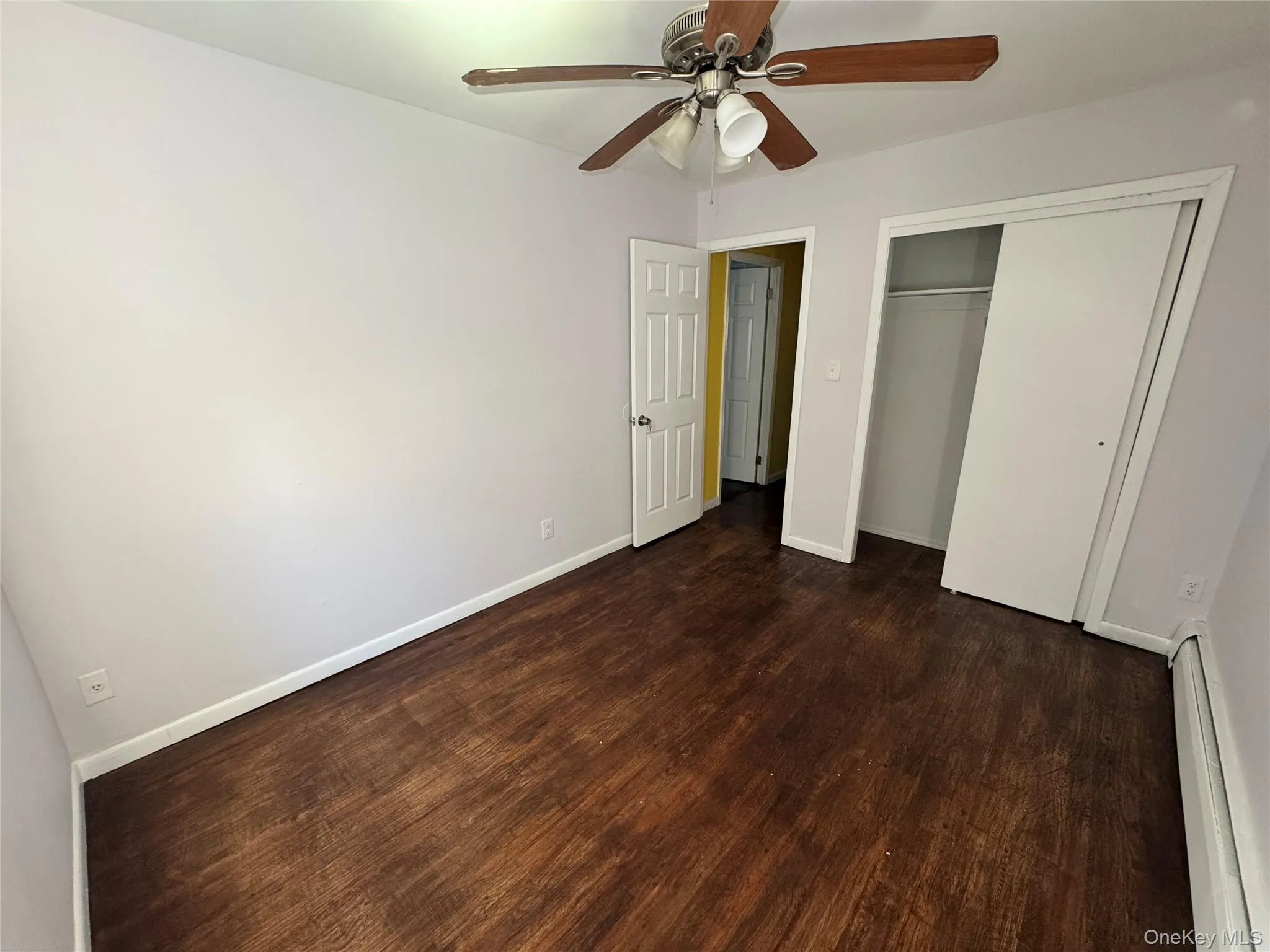 Unfurnished bedroom with a baseboard heating unit, dark wood-style flooring, a closet, and a ceiling fan Unfurnished bedroom with a baseboard heating unit, dark wood-style flooring, a closet, and a ceiling fan