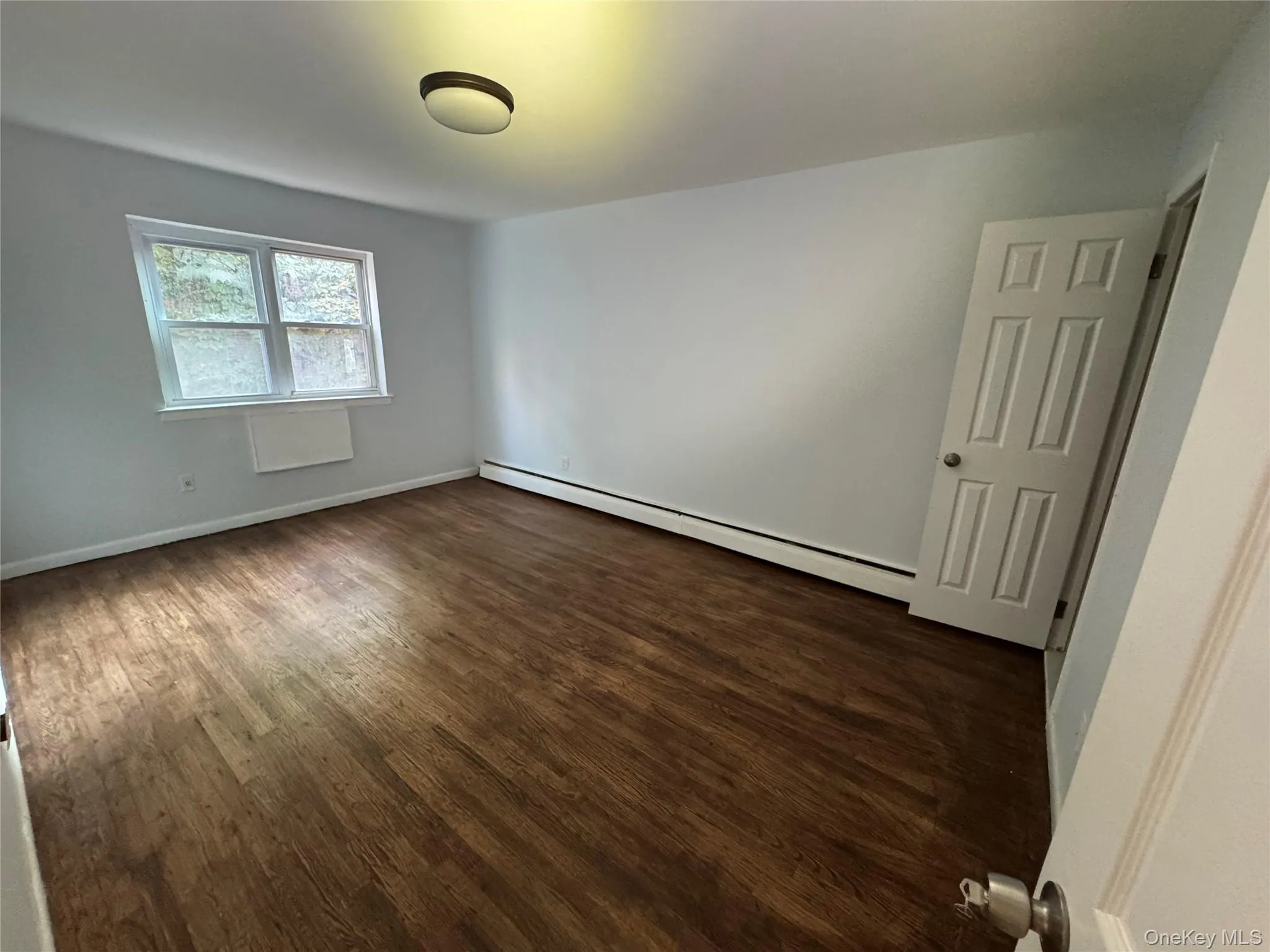 Unfurnished room featuring dark wood-style flooring and a baseboard heating unit Unfurnished room featuring dark wood-style flooring and a baseboard heating unit
