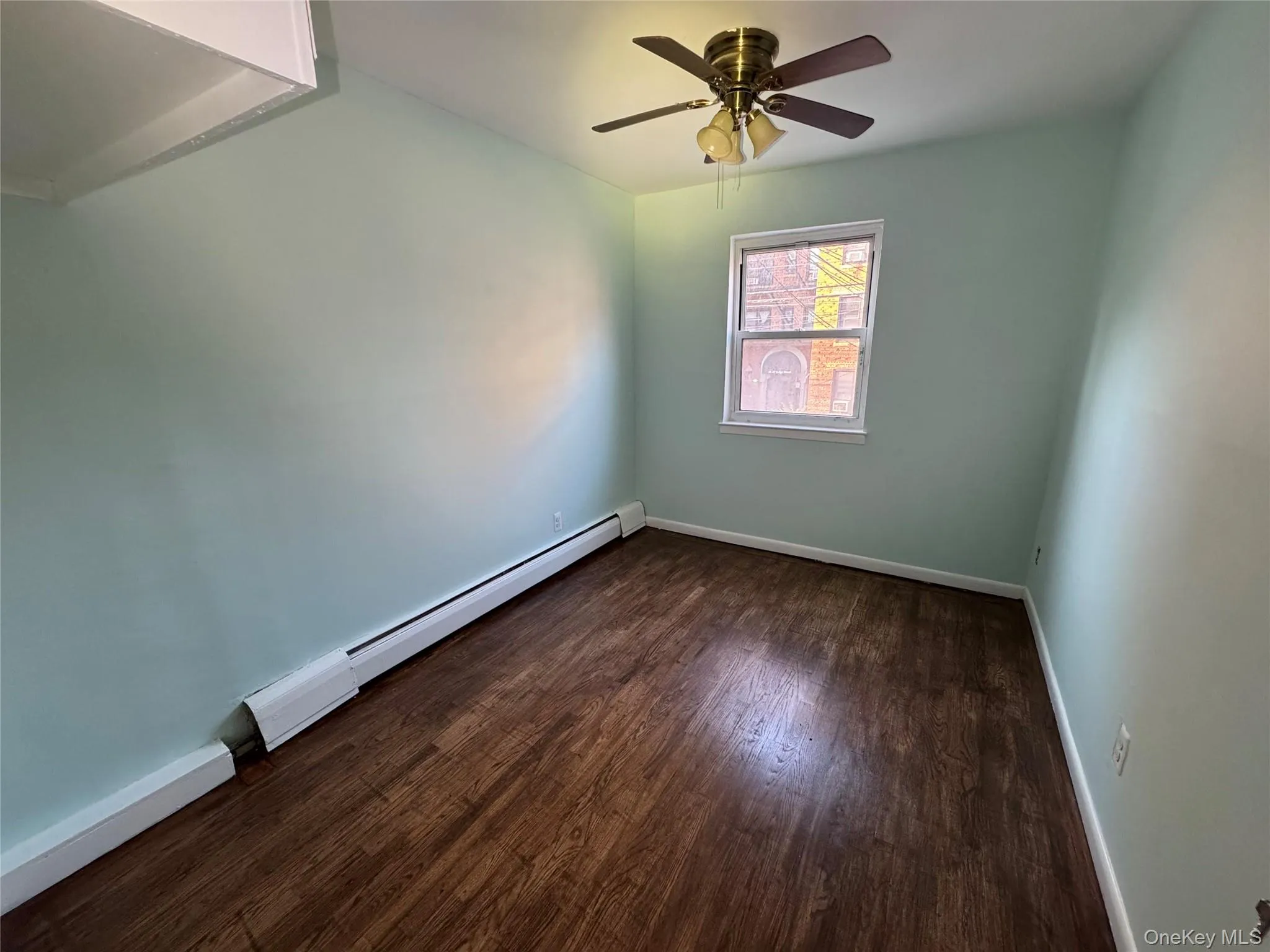 Unfurnished room featuring baseboard heating, dark wood finished floors, and a ceiling fan Unfurnished room featuring baseboard heating, dark wood finished floors, and a ceiling fan