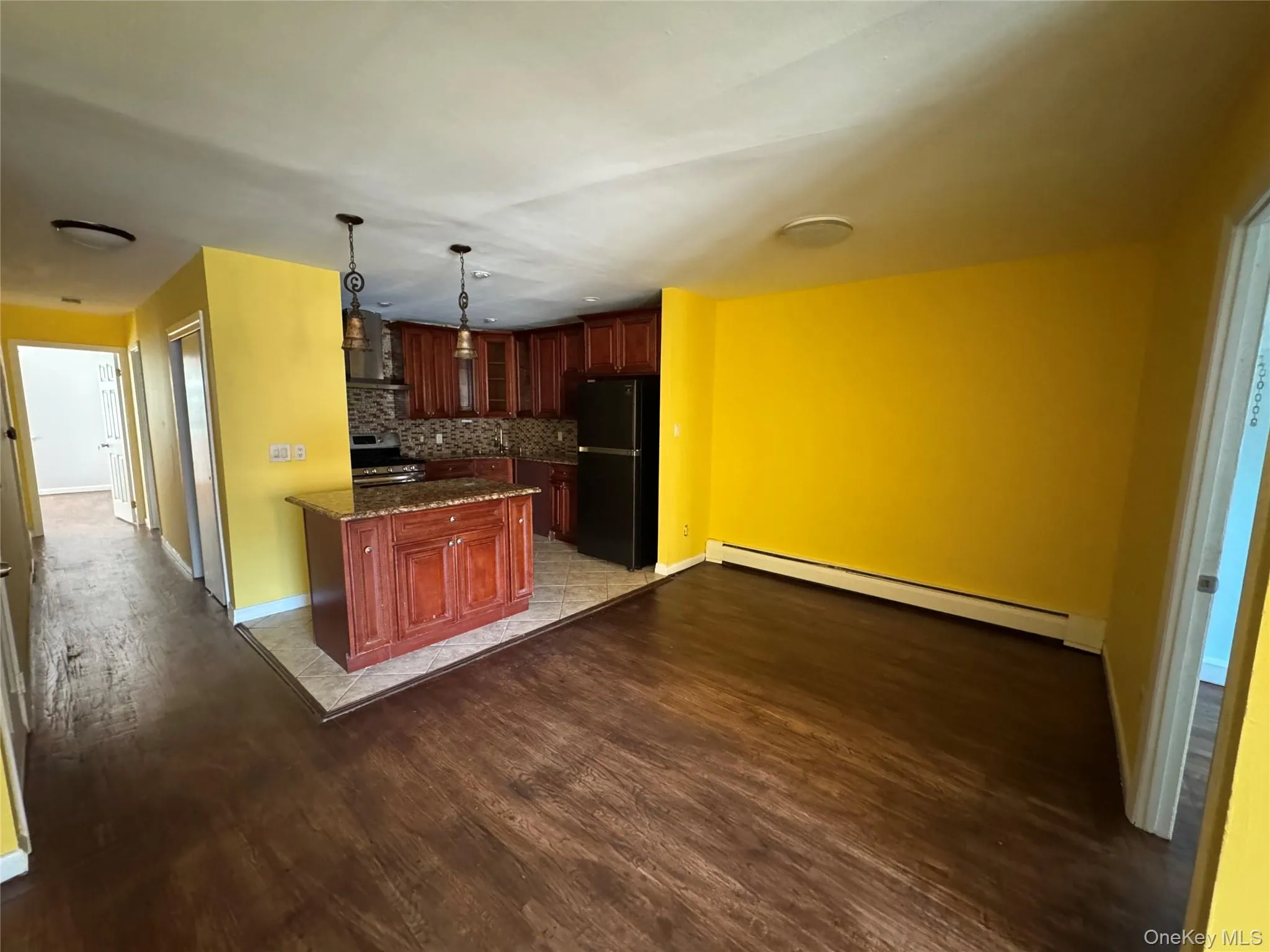 Kitchen with baseboard heating, freestanding refrigerator, dark stone countertops, glass insert cabinets, and dark wood finished floors Kitchen with baseboard heating, freestanding refrigerator, dark stone countertops, glass insert cabinets, and dark wood finished floors