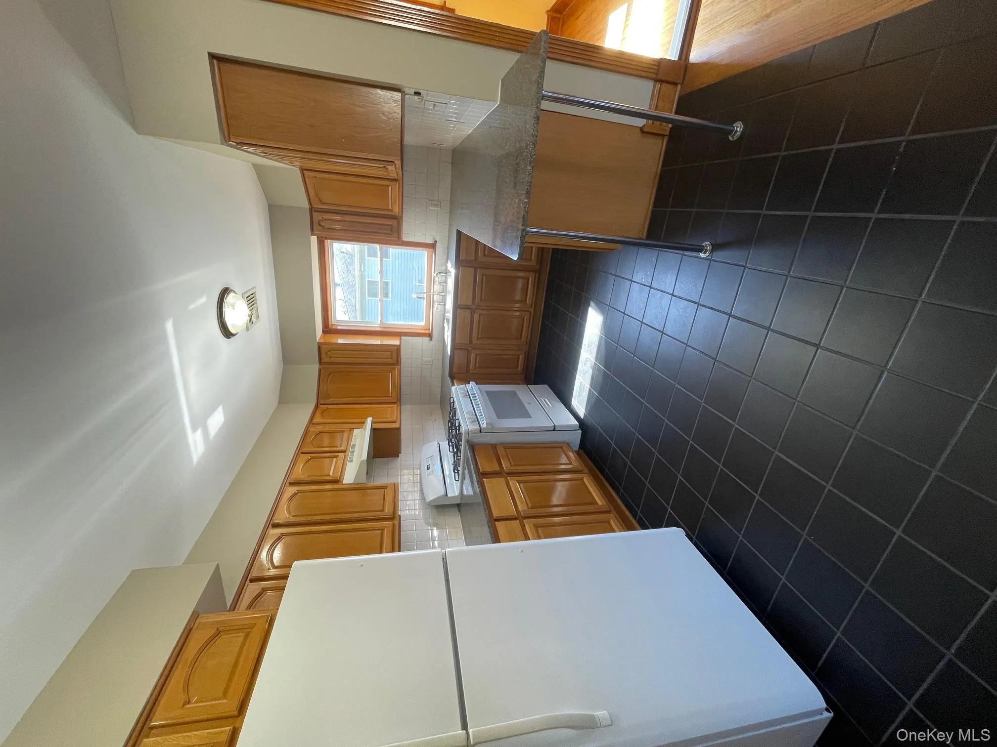 Kitchen featuring refrigerator, white range with gas stovetop, backsplash, dark tile patterned flooring, and range hood Kitchen featuring refrigerator, white range with gas stovetop, backsplash, dark tile patterned flooring, and range hood