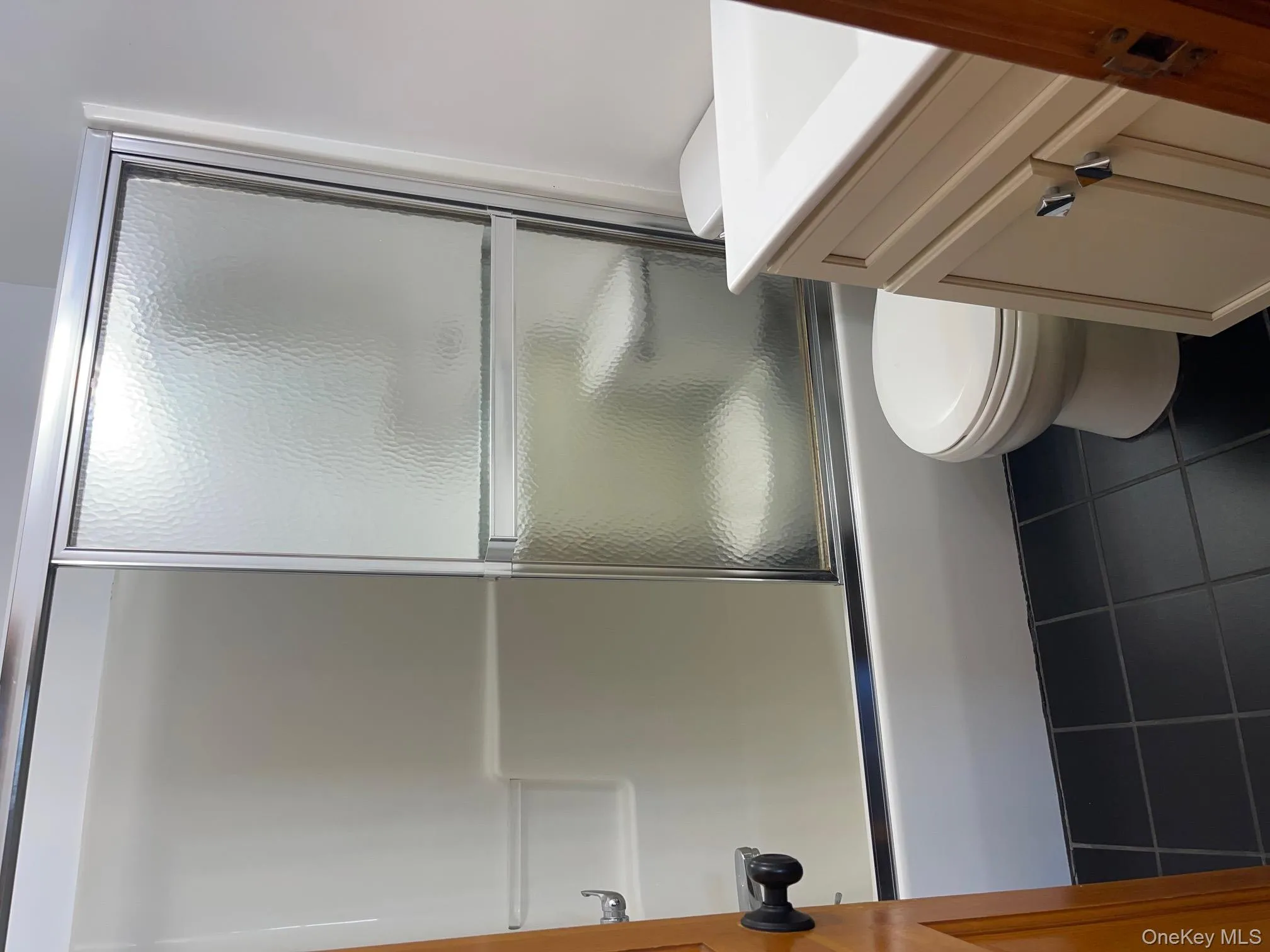 Full bathroom with vanity, shower / bath combination with glass door, and dark tile patterned floors Full bathroom with vanity, shower / bath combination with glass door, and dark tile patterned floors