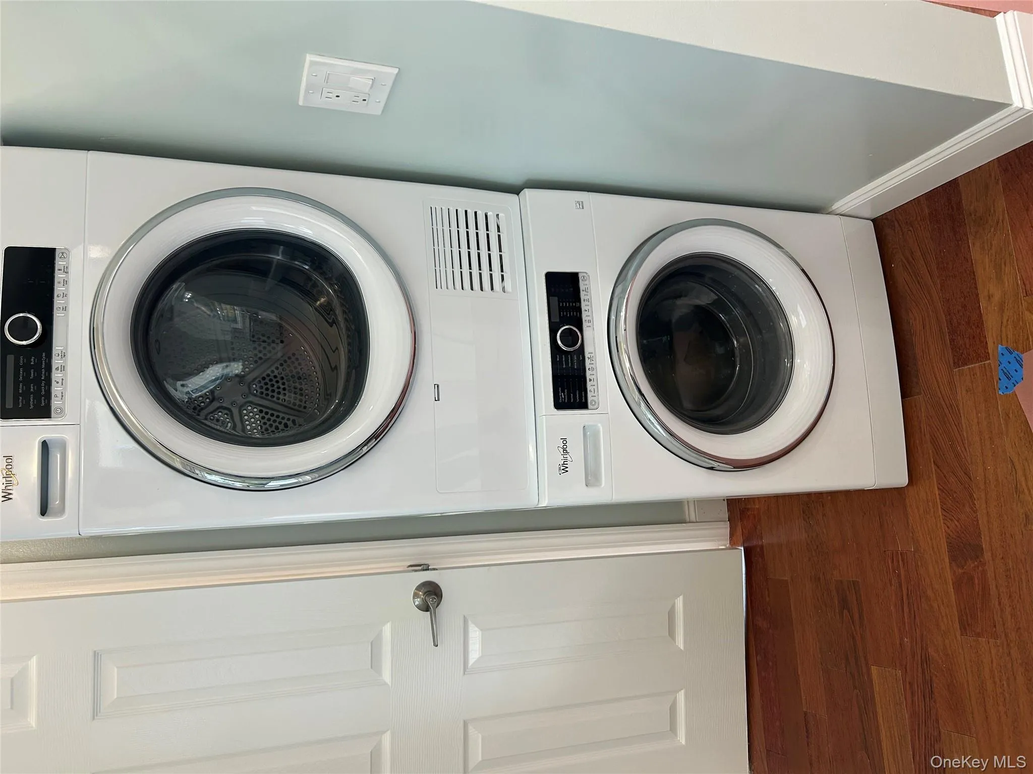 Washroom featuring dark wood finished floors and stacked washer and clothes dryer Washroom featuring dark wood finished floors and stacked washer and clothes dryer
