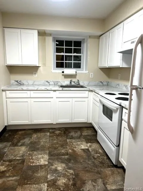 Kitchen with white cabinets, white appliances, stone finish flooring, and exhaust hood Kitchen with white cabinets, white appliances, stone finish flooring, and exhaust hood