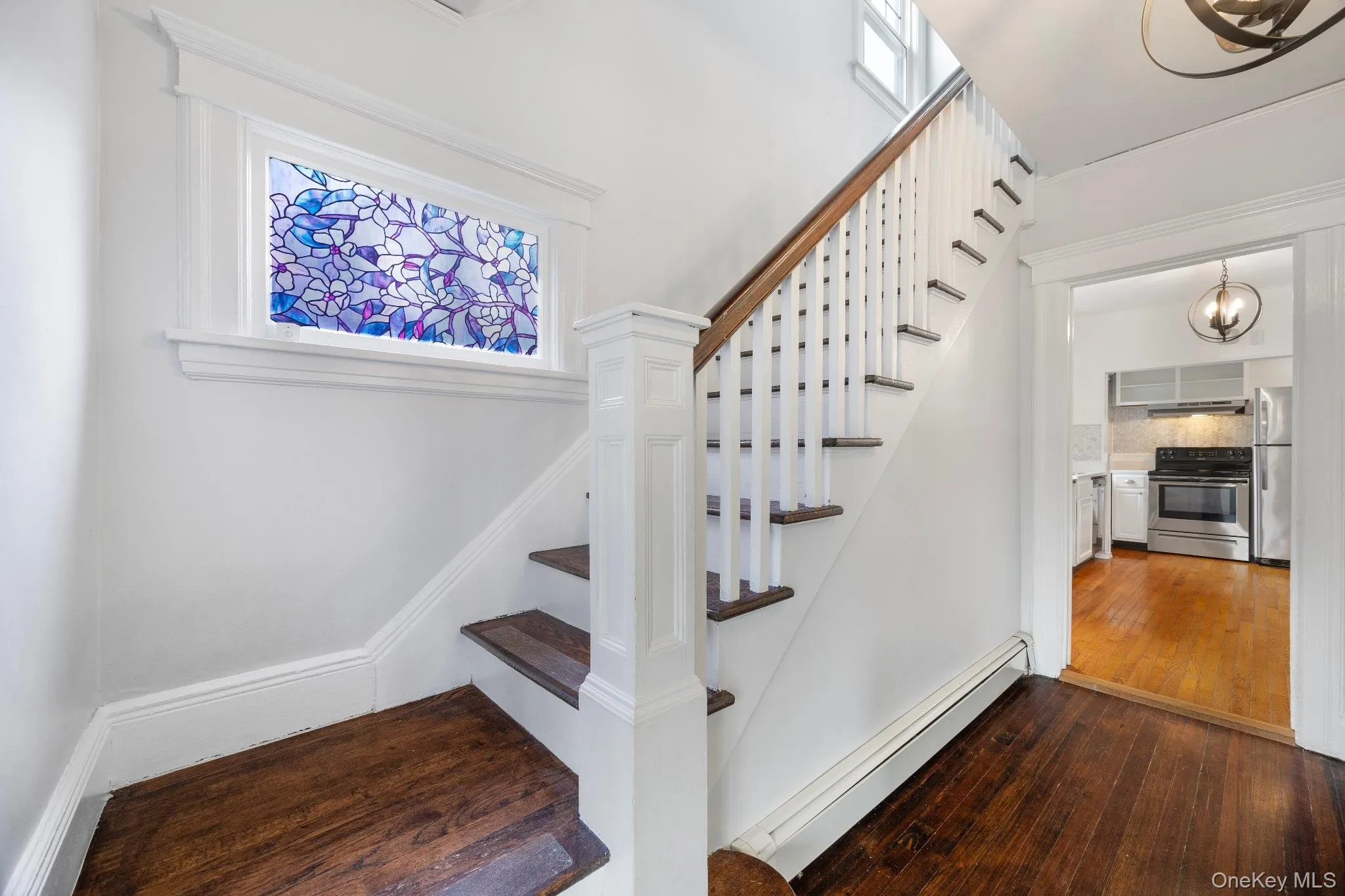 Stairway featuring baseboard heating, hardwood / wood-style flooring, and a chandelier Stairway featuring baseboard heating, hardwood / wood-style flooring, and a chandelier
