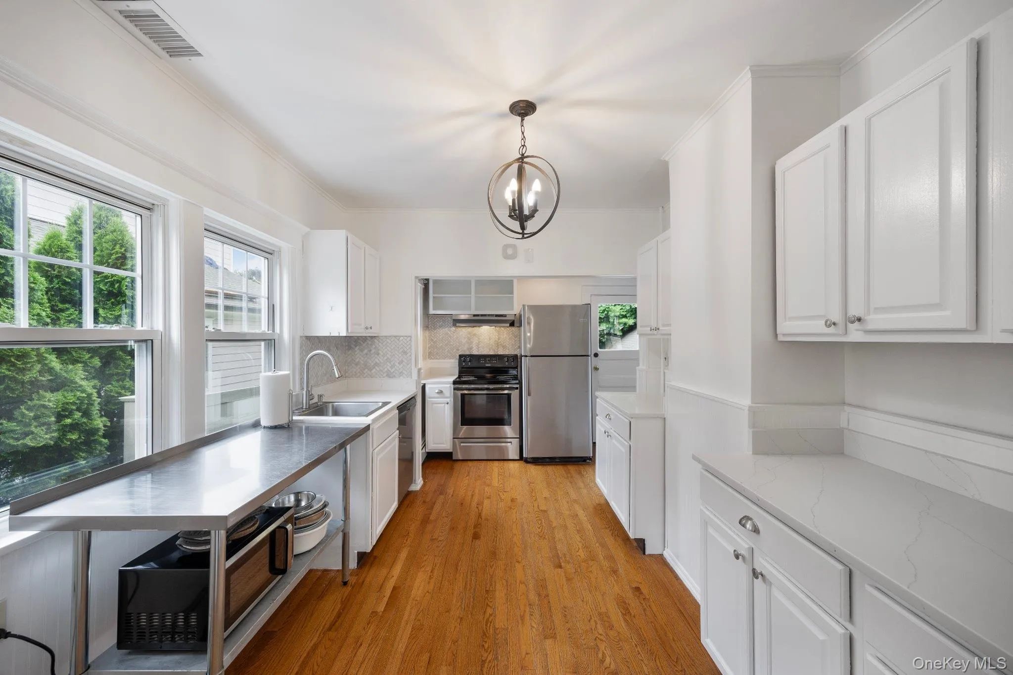 Kitchen with white cabinets, stainless steel appliances, light wood-style floors, tasteful backsplash, and pendant lighting Kitchen with white cabinets, stainless steel appliances, light wood-style floors, tasteful backsplash, and pendant lighting