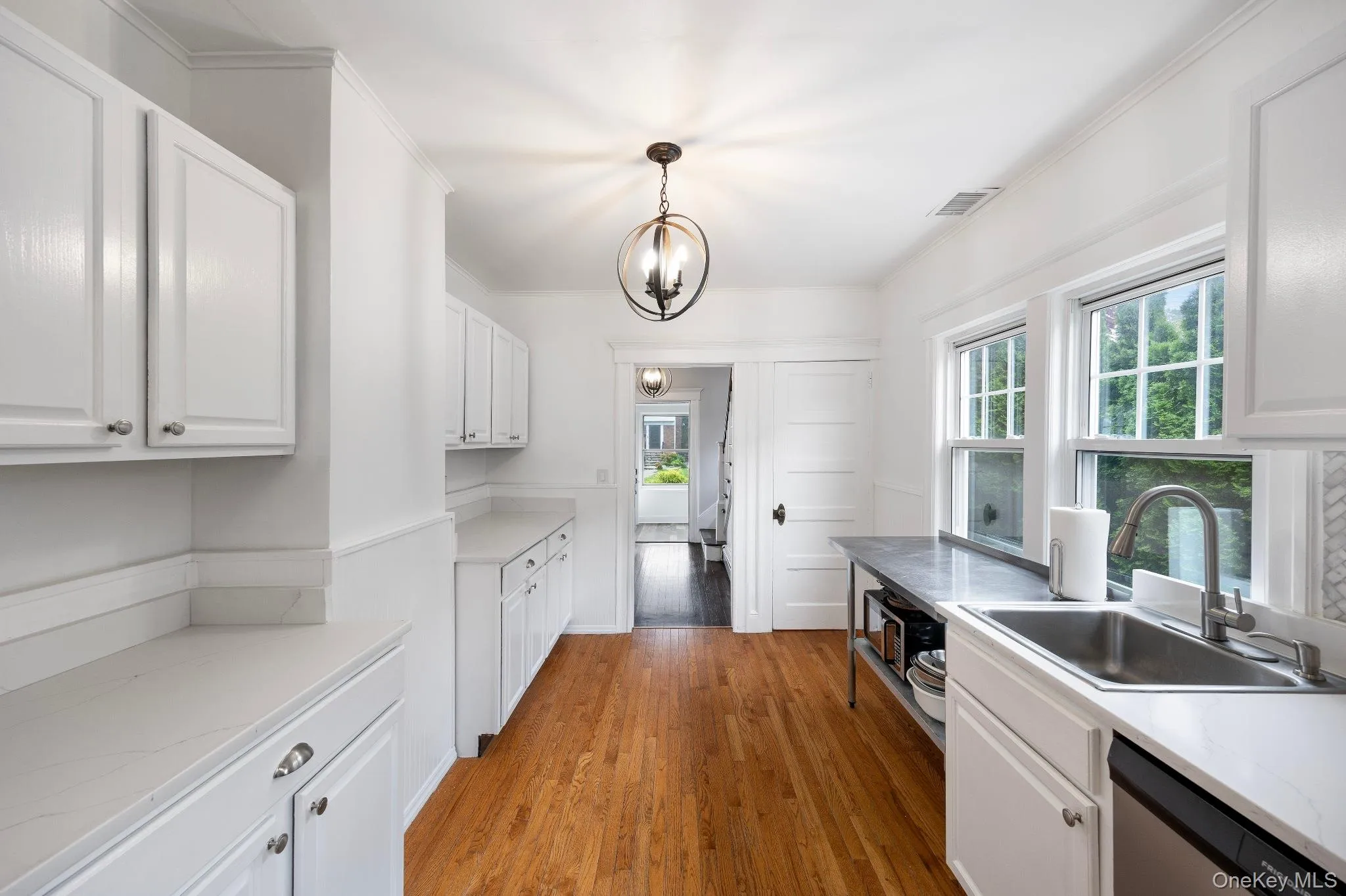 Kitchen with light countertops, white cabinets, light wood-type flooring, and crown molding Kitchen with light countertops, white cabinets, light wood-type flooring, and crown molding