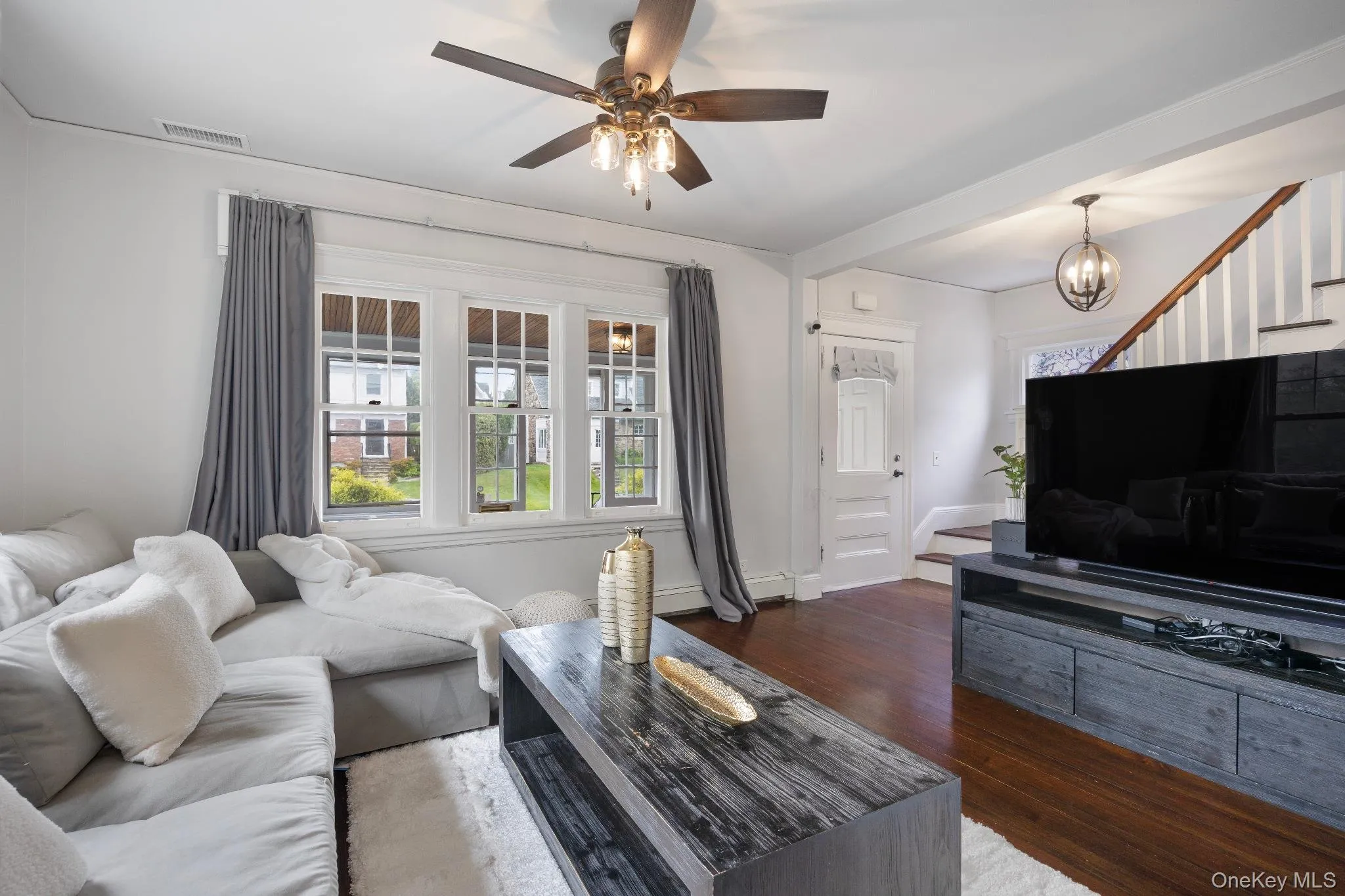 Living area featuring dark wood-style flooring, stairway, a ceiling fan, and a chandelier Living area featuring dark wood-style flooring, stairway, a ceiling fan, and a chandelier