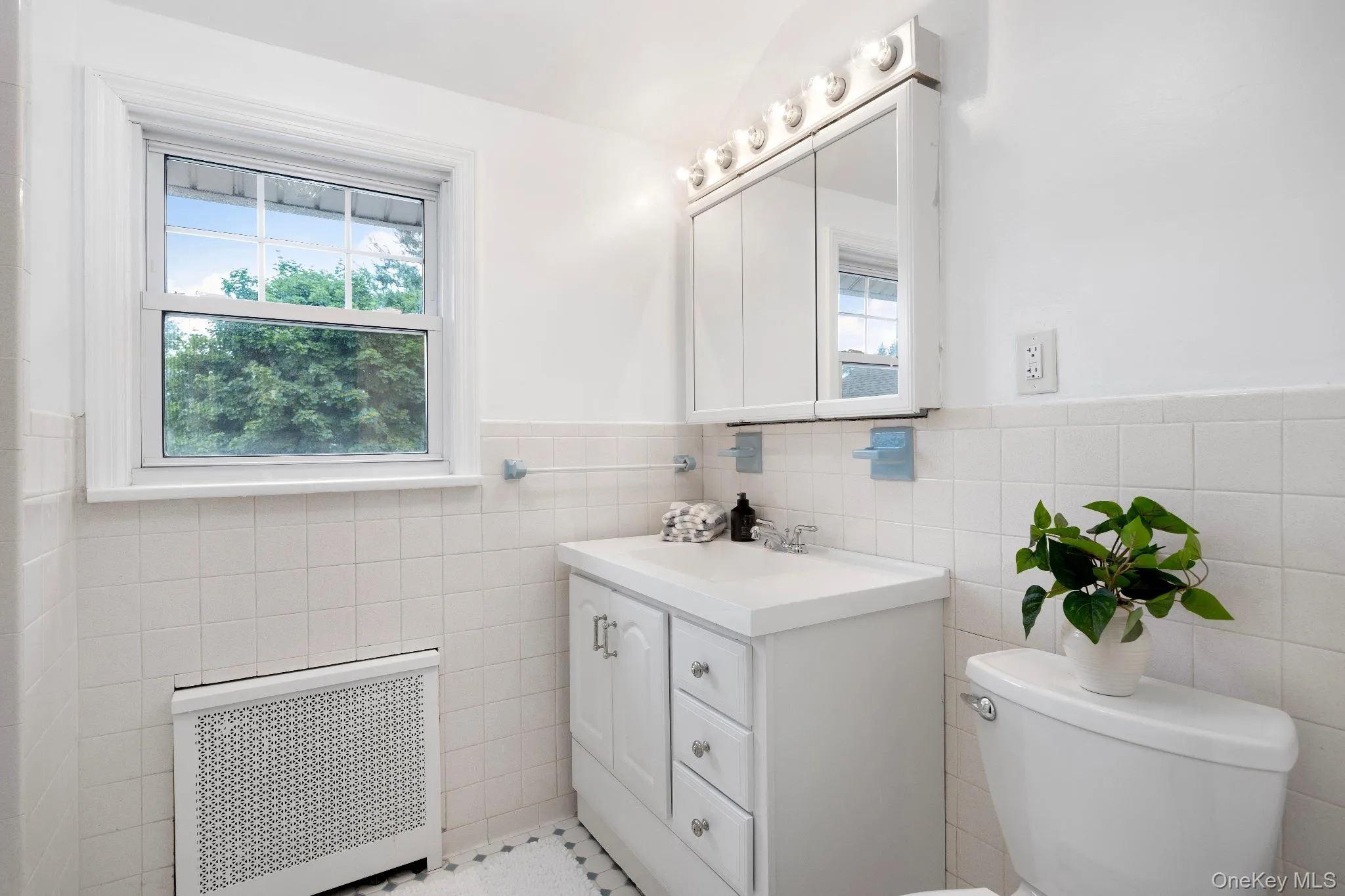 Bathroom featuring radiator heating unit, vanity, healthy amount of natural light, tile walls, and wainscoting Bathroom featuring radiator heating unit, vanity, healthy amount of natural light, tile walls, and wainscoting