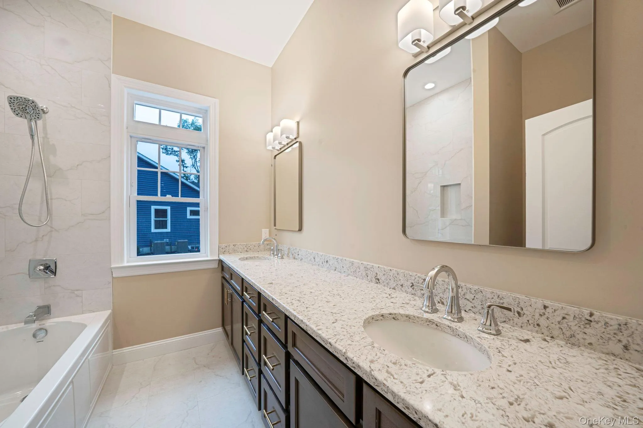 Bathroom featuring double vanity, light marble finish floors, and a combined bath / shower with marble appearance Bathroom featuring double vanity, light marble finish floors, and a combined bath / shower with marble appearance