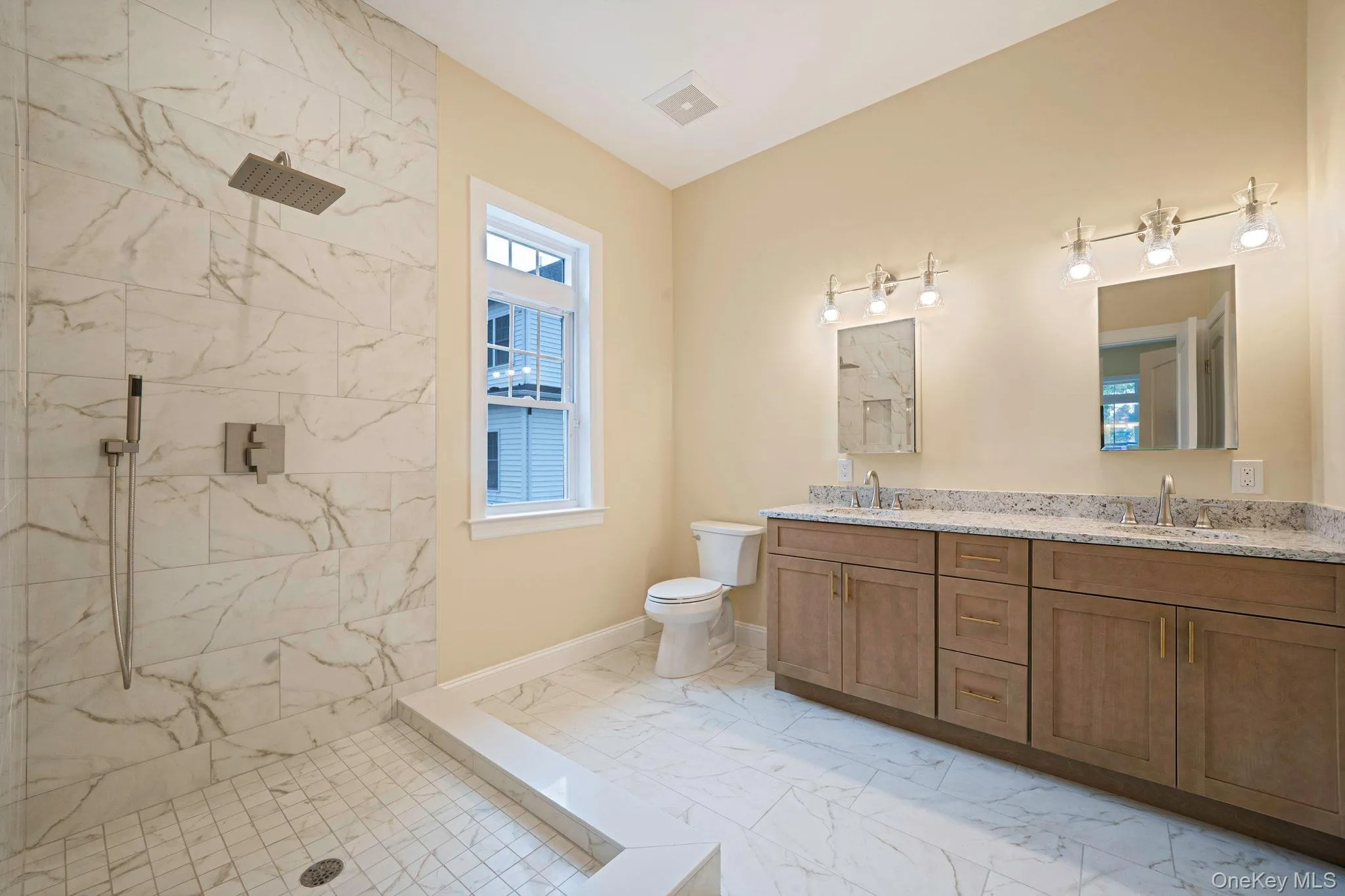 Full bathroom featuring double vanity, a marble finish shower, and light marble finish floors Full bathroom featuring double vanity, a marble finish shower, and light marble finish floors