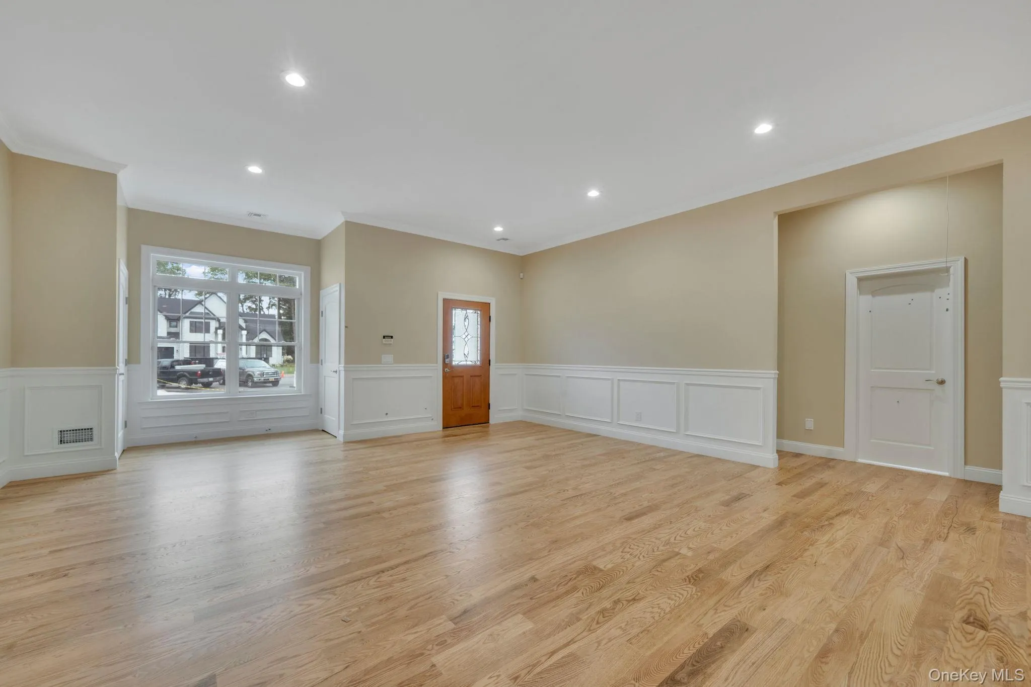 Unfurnished living room featuring wainscoting, recessed lighting, light wood-style floors, ornamental molding, and a decorative wall Unfurnished living room featuring wainscoting, recessed lighting, light wood-style floors, ornamental molding, and a decorative wall