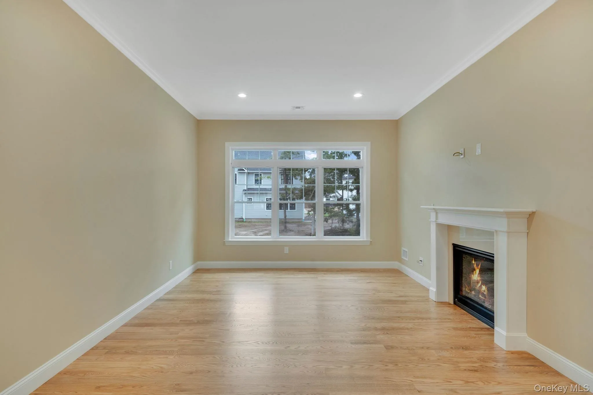 Unfurnished living room with a glass covered fireplace, light wood-type flooring, ornamental molding, and recessed lighting Unfurnished living room with a glass covered fireplace, light wood-type flooring, ornamental molding, and recessed lighting