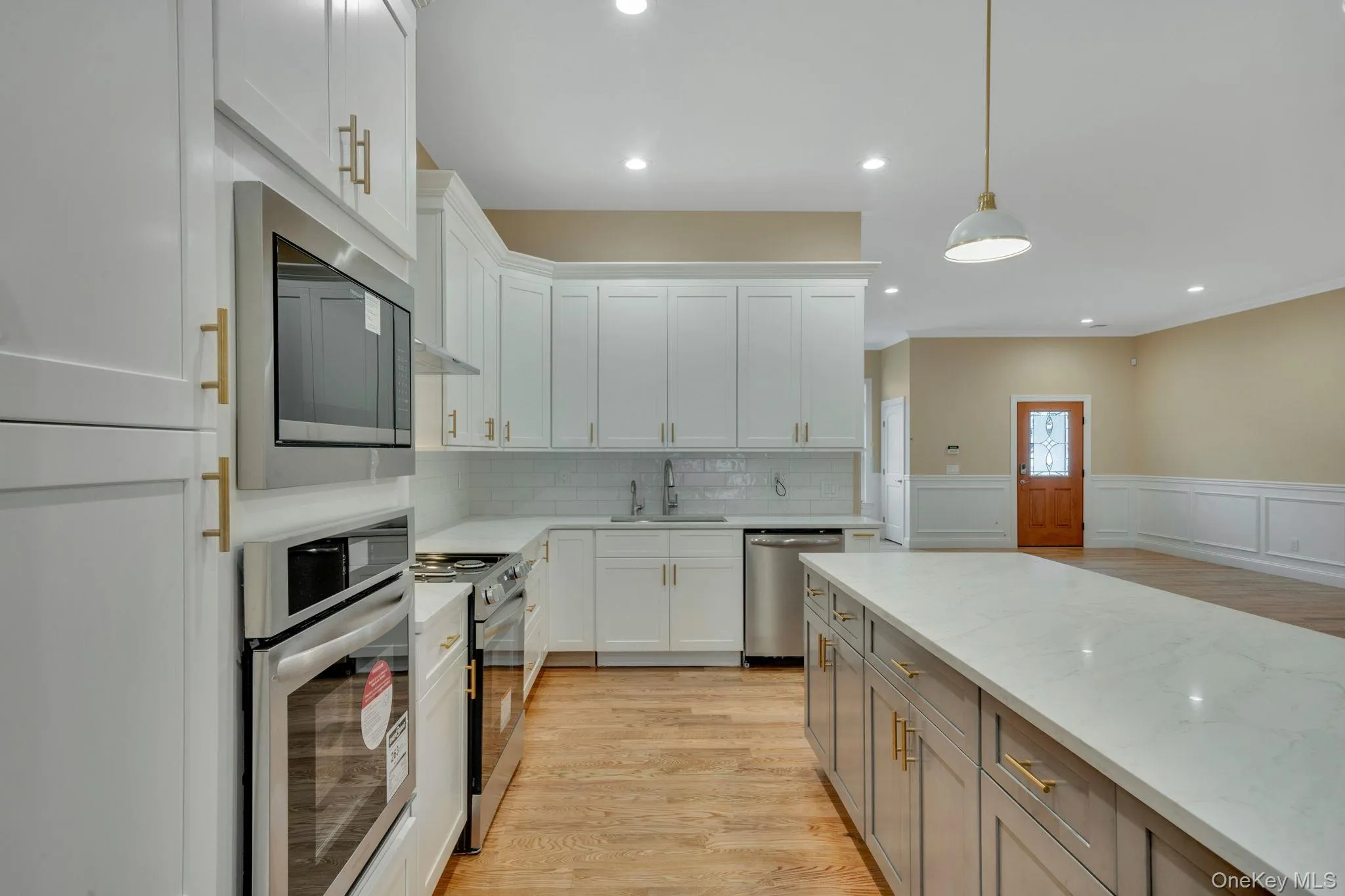 Kitchen featuring a wainscoted wall, appliances with stainless steel finishes, light wood-type flooring, light stone countertops, and hanging light fixtures Kitchen featuring a wainscoted wall, appliances with stainless steel finishes, light wood-type flooring, light stone countertops, and hanging light fixtures