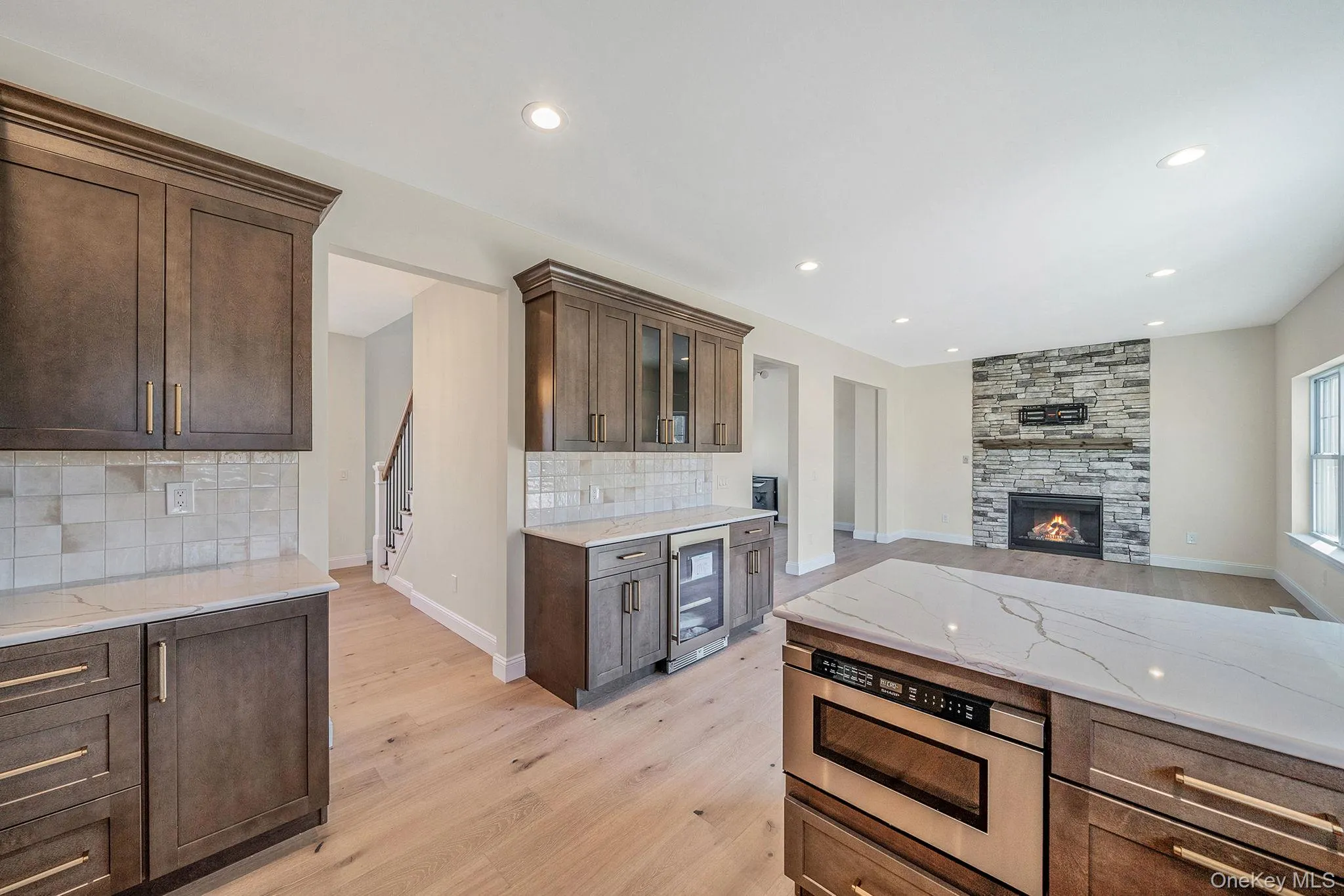 Kitchen featuring light stone countertops, dark brown cabinets, backsplash, a stone fireplace, and light wood finished floors Kitchen featuring light stone countertops, dark brown cabinets, backsplash, a stone fireplace, and light wood finished floors