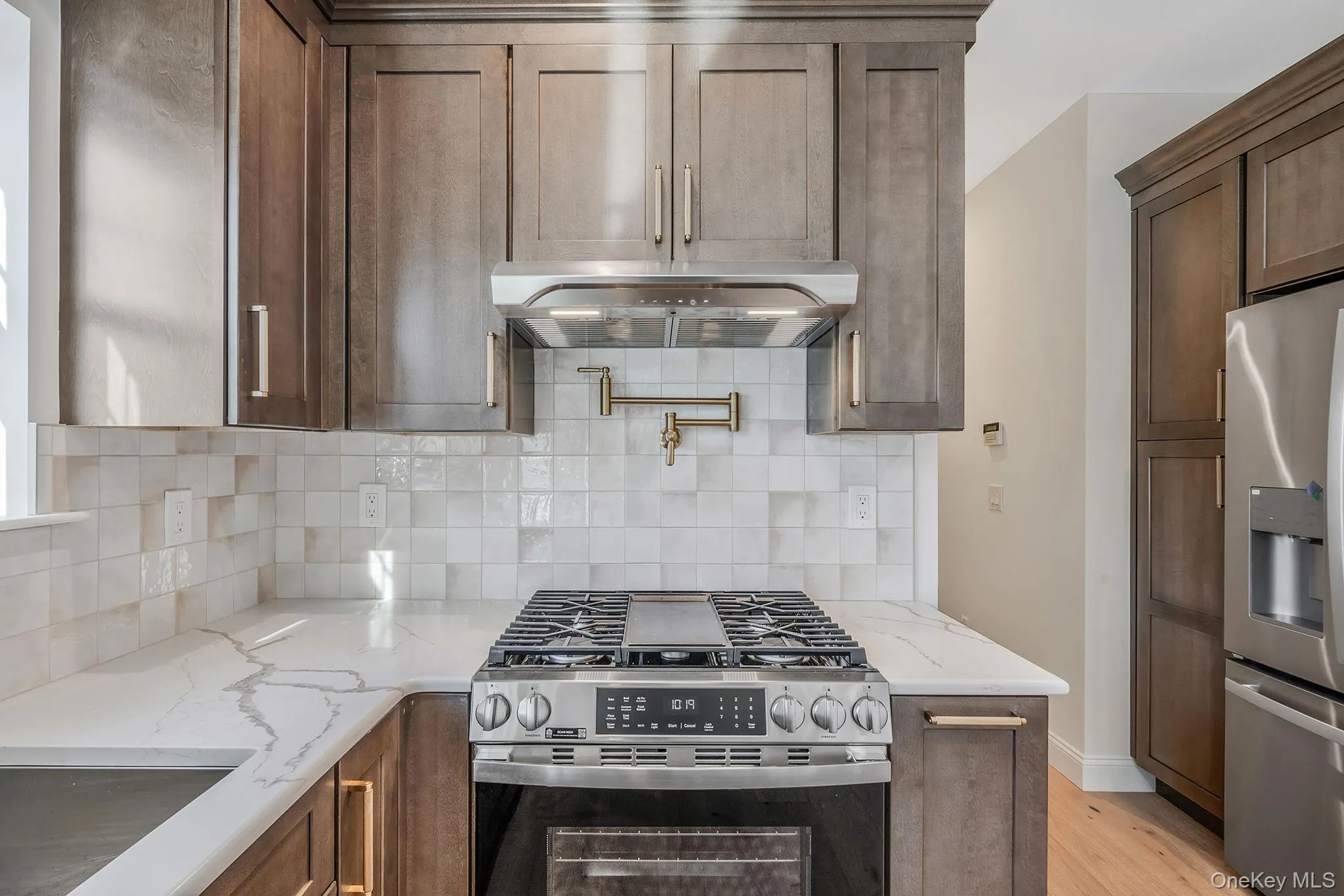Kitchen with appliances with stainless steel finishes, light stone counters, exhaust hood, tasteful backsplash, and light wood-type flooring Kitchen with appliances with stainless steel finishes, light stone counters, exhaust hood, tasteful backsplash, and light wood-type flooring