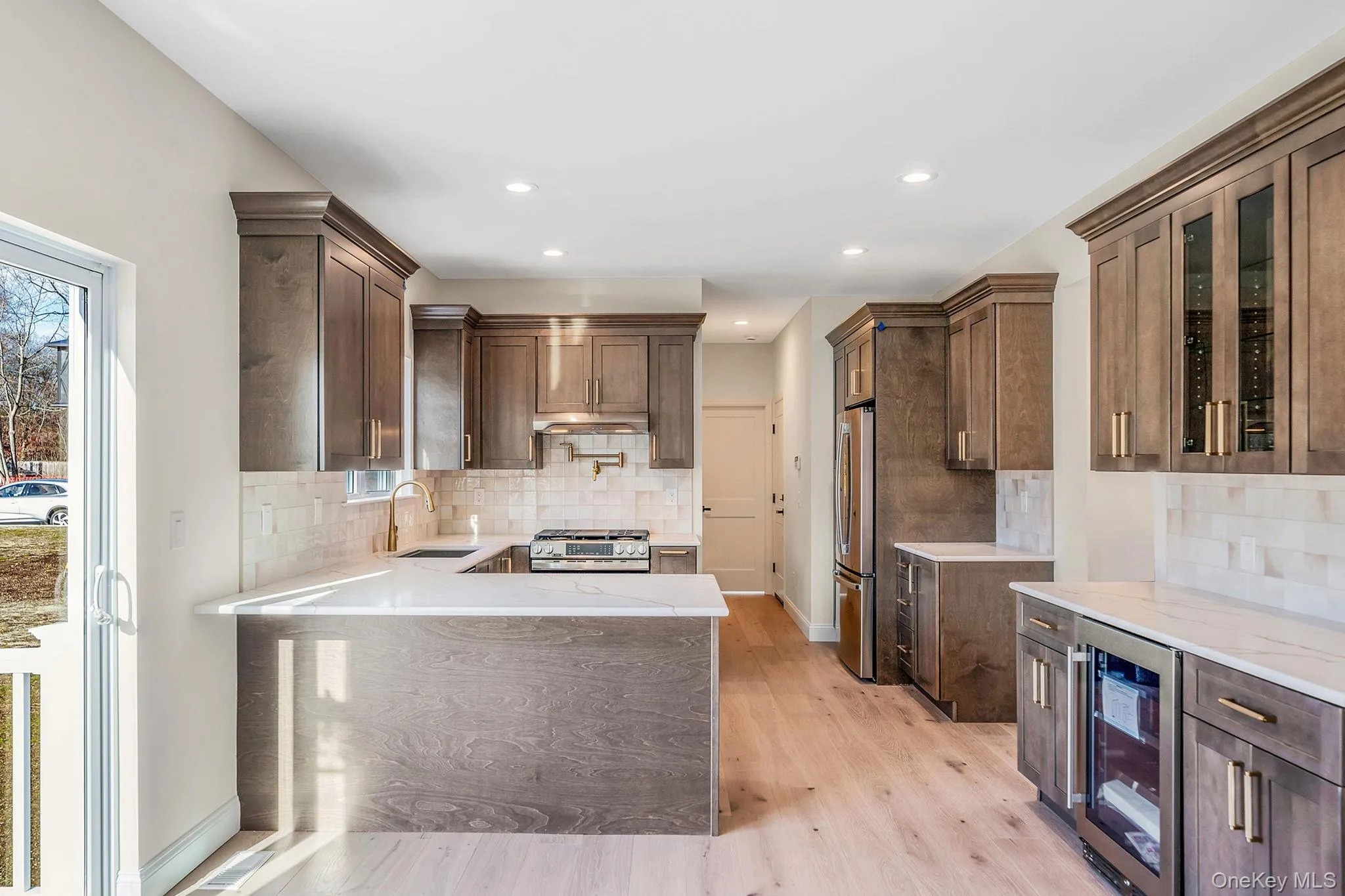 Kitchen with light stone countertops, a peninsula, beverage cooler, glass insert cabinets, and recessed lighting Kitchen with light stone countertops, a peninsula, beverage cooler, glass insert cabinets, and recessed lighting