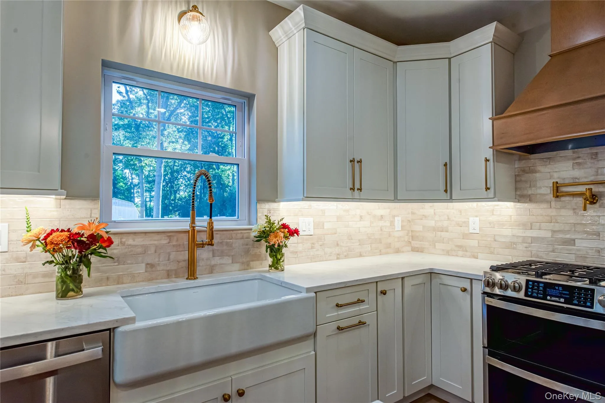 Kitchen with appliances with stainless steel finishes, custom exhaust hood, light stone counters, white cabinets, and decorative light fixtures Kitchen with appliances with stainless steel finishes, custom exhaust hood, light stone counters, white cabinets, and decorative light fixtures