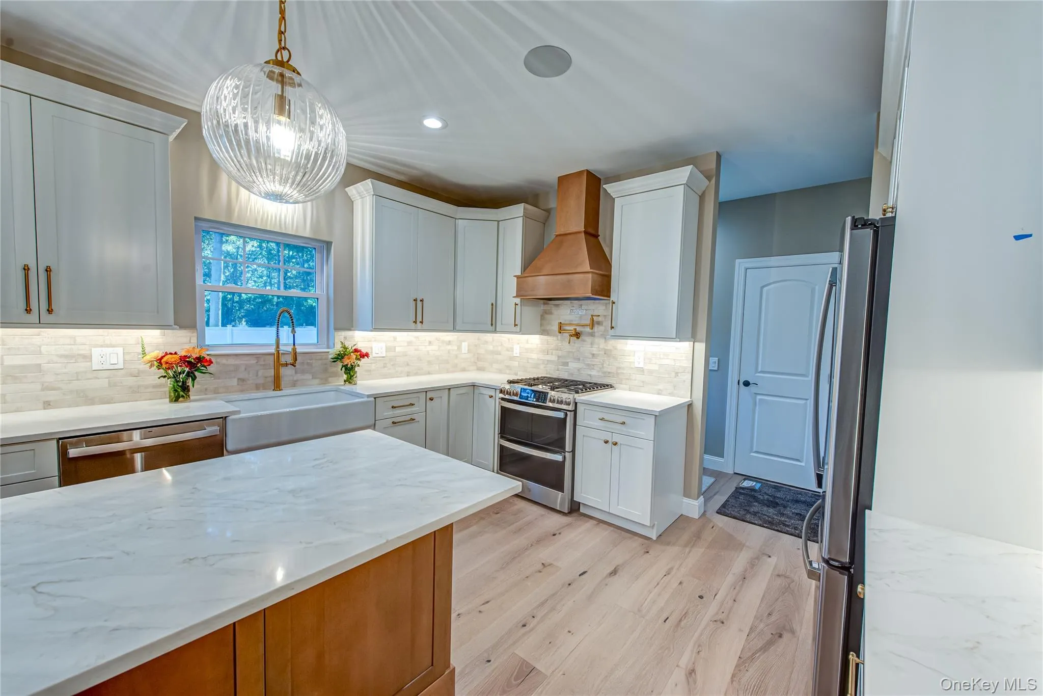 Kitchen with recessed lighting, light stone countertops, appliances with stainless steel finishes, light wood finished floors, and custom range hood Kitchen with recessed lighting, light stone countertops, appliances with stainless steel finishes, light wood finished floors, and custom range hood