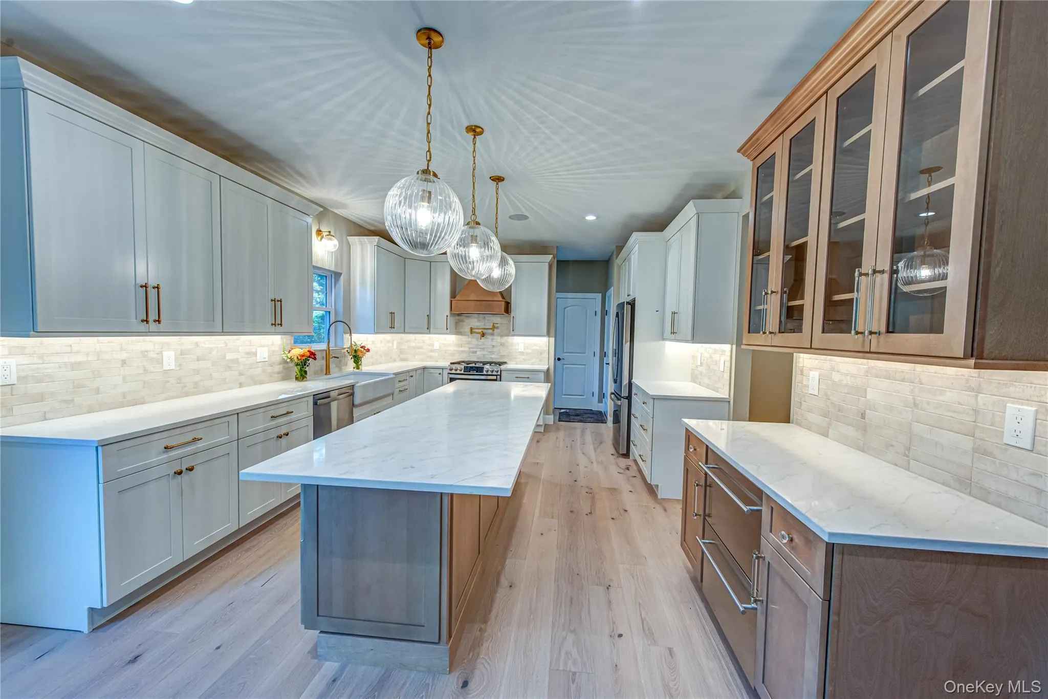 Kitchen with a kitchen island, light stone counters, pendant lighting, glass insert cabinets, and light wood finished floors Kitchen with a kitchen island, light stone counters, pendant lighting, glass insert cabinets, and light wood finished floors