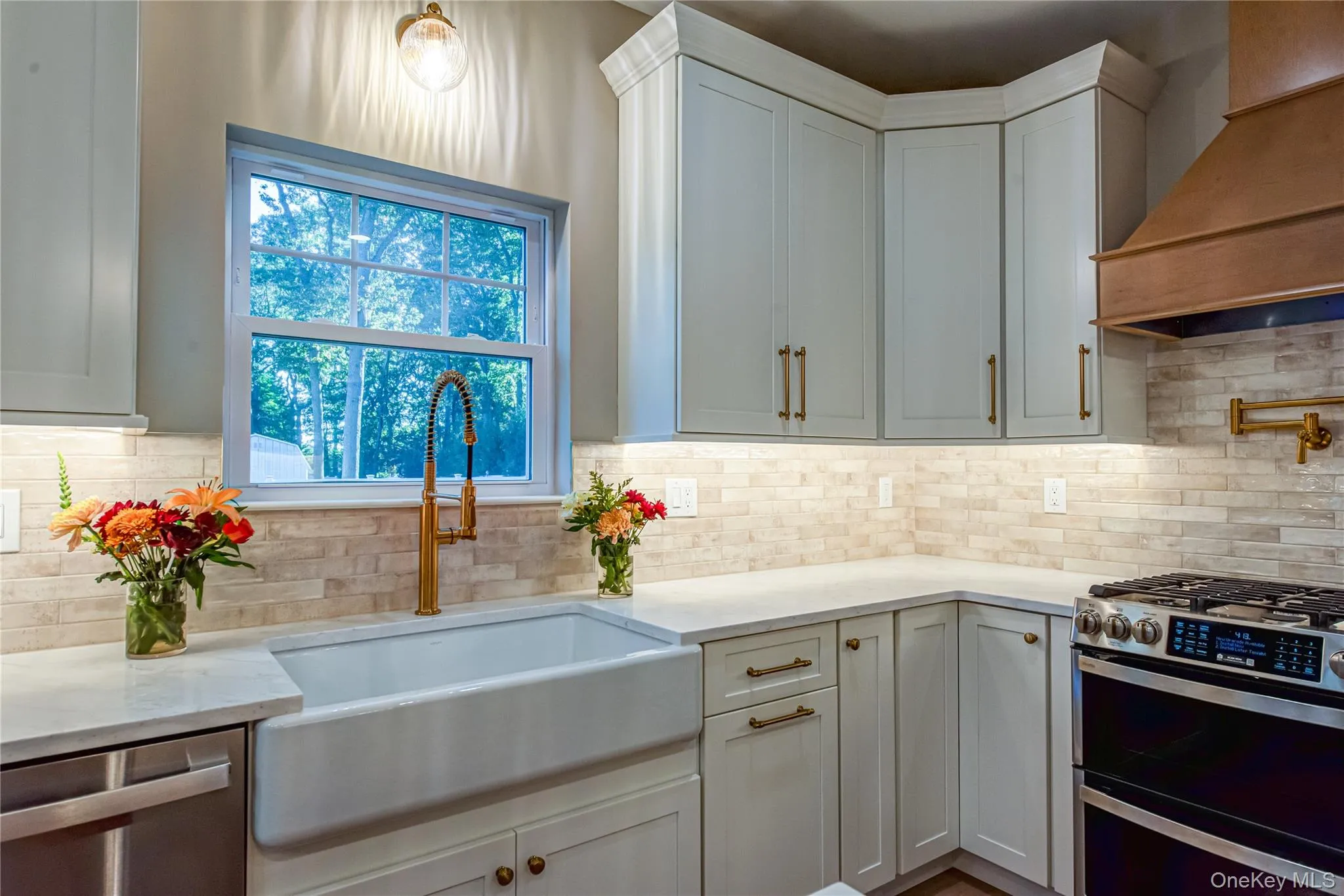 Kitchen featuring stainless steel appliances, custom range hood, light stone countertops, white cabinets, and backsplash Kitchen featuring stainless steel appliances, custom range hood, light stone countertops, white cabinets, and backsplash