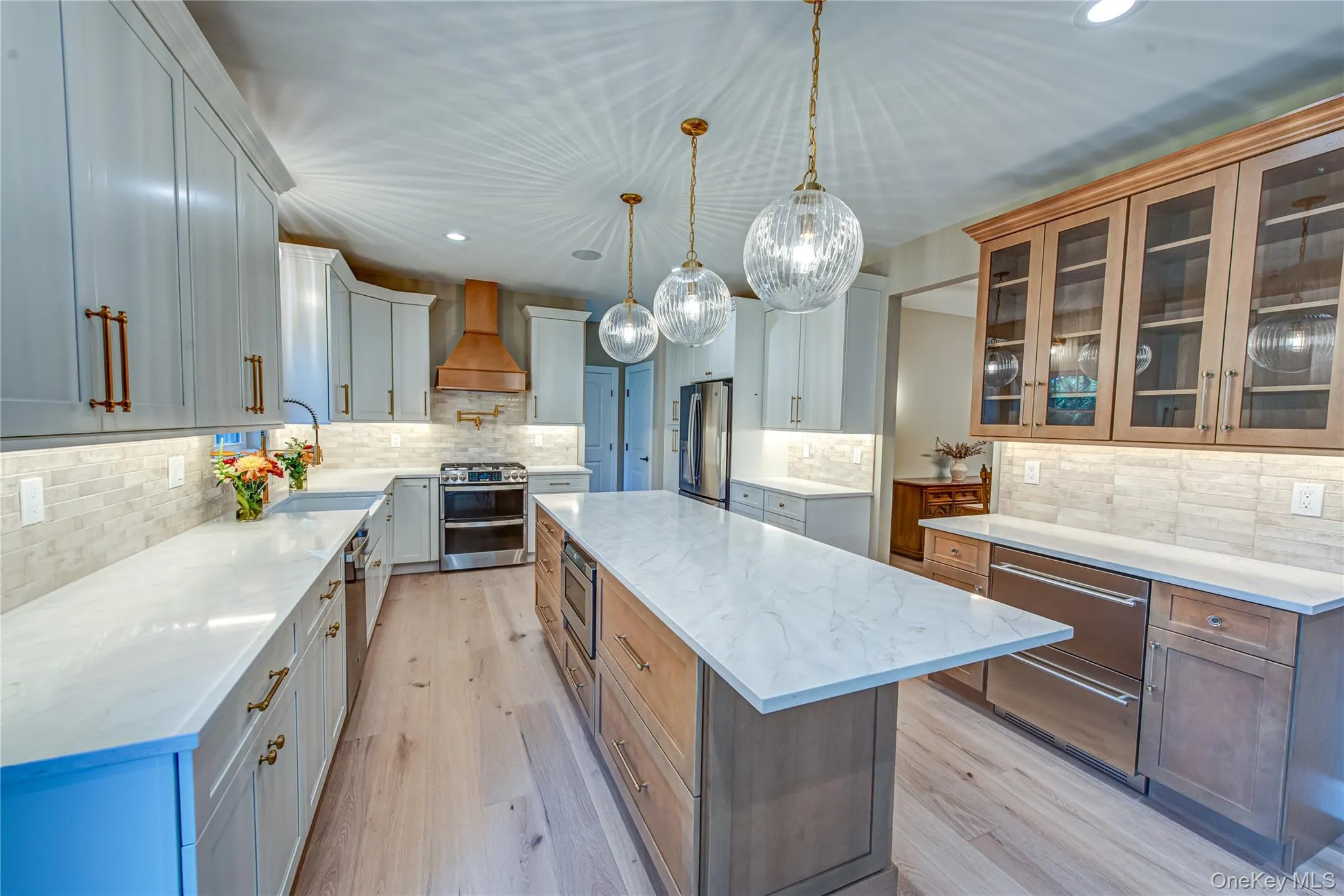 Kitchen featuring recessed lighting, a center island, glass insert cabinets, light stone counters, and light wood-style flooring Kitchen featuring recessed lighting, a center island, glass insert cabinets, light stone counters, and light wood-style flooring