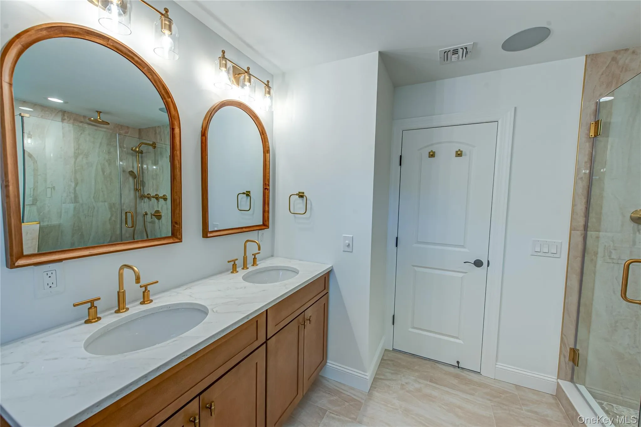 Full bathroom with a marble finish shower, double vanity, and light tile patterned flooring Full bathroom with a marble finish shower, double vanity, and light tile patterned flooring
