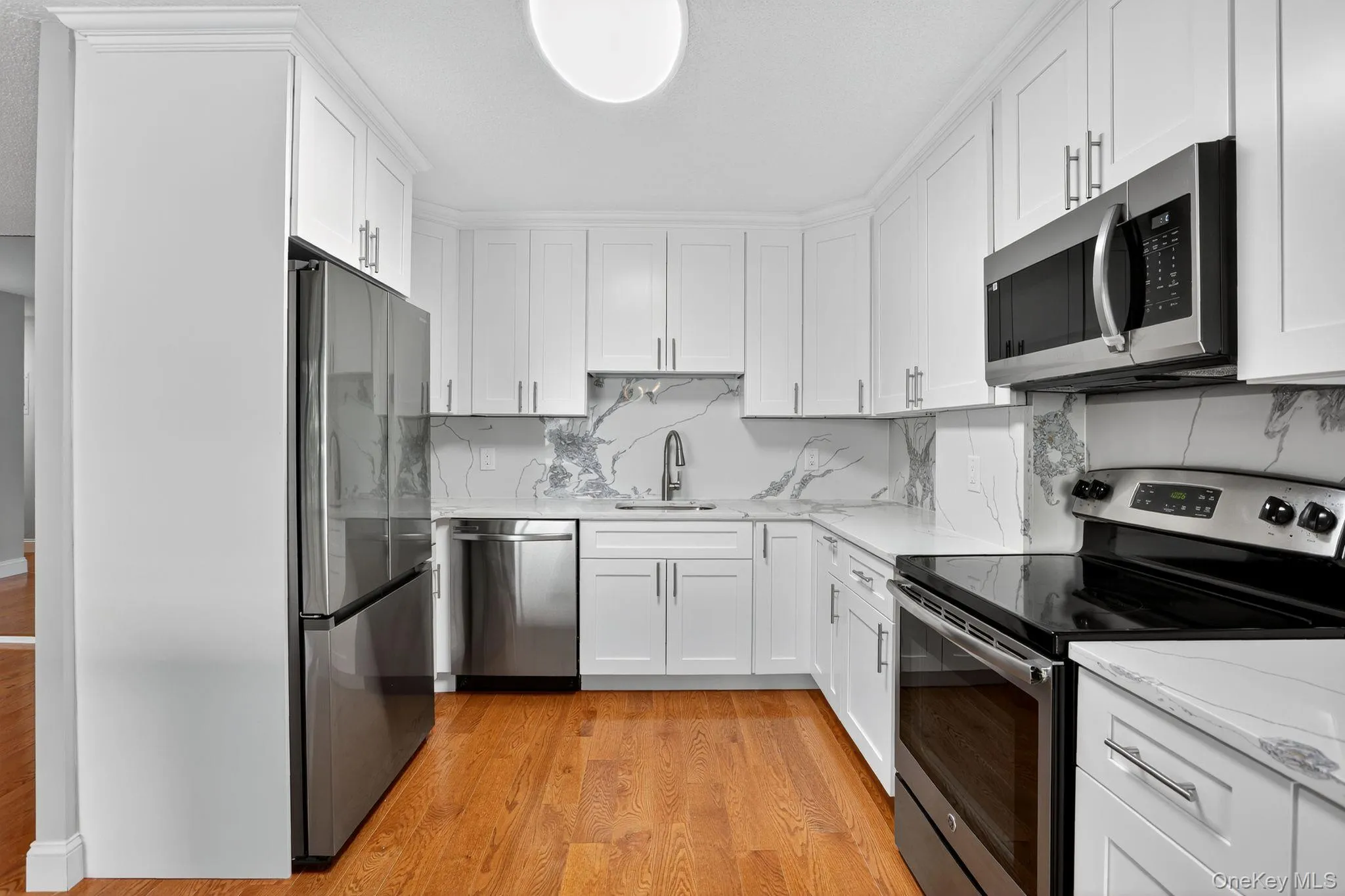 Kitchen featuring appliances with stainless steel finishes, tasteful backsplash, light wood-type flooring, white cabinets, and light stone countertops Kitchen featuring appliances with stainless steel finishes, tasteful backsplash, light wood-type flooring, white cabinets, and light stone countertops